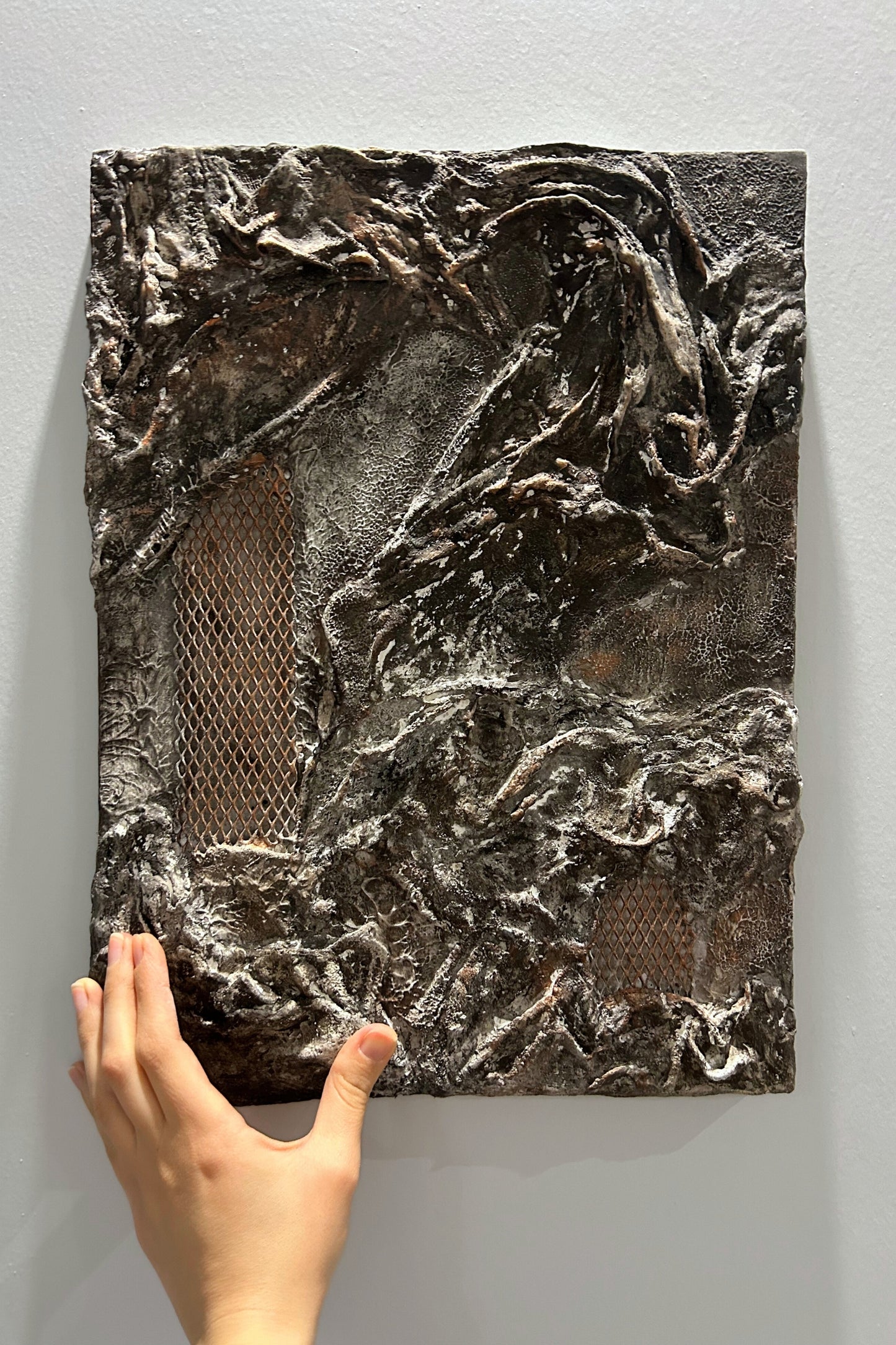 Sculptural abstract wall art held by hand against a neutral background.