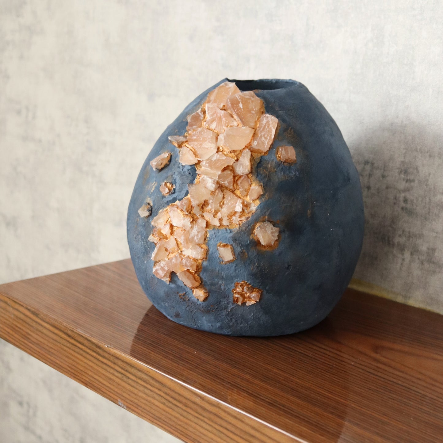 Textured blue vase placed on wooden shelf in rustic interior setting