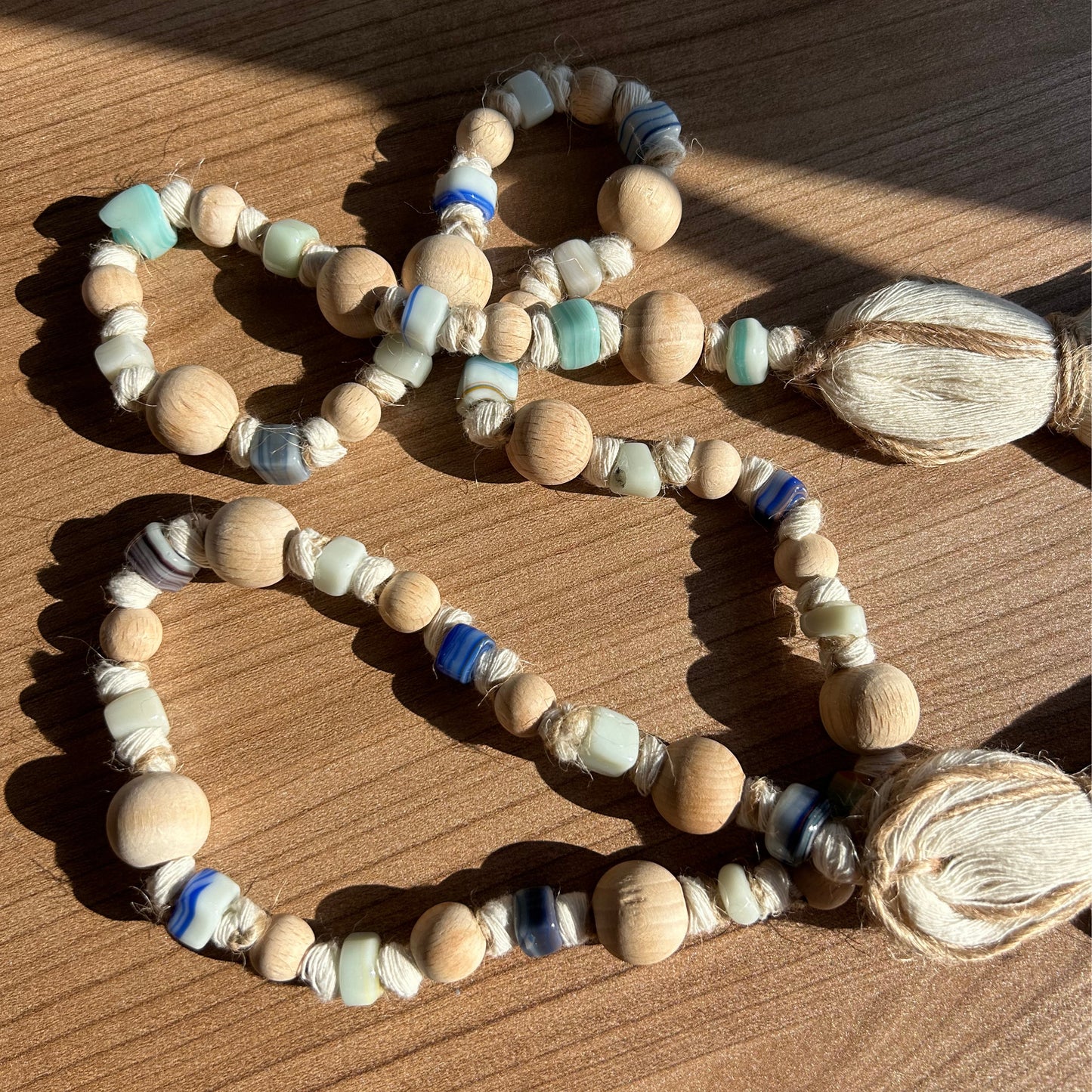 Flatlay of handmade wood and glass bead garland styled with tassels in natural lighting.