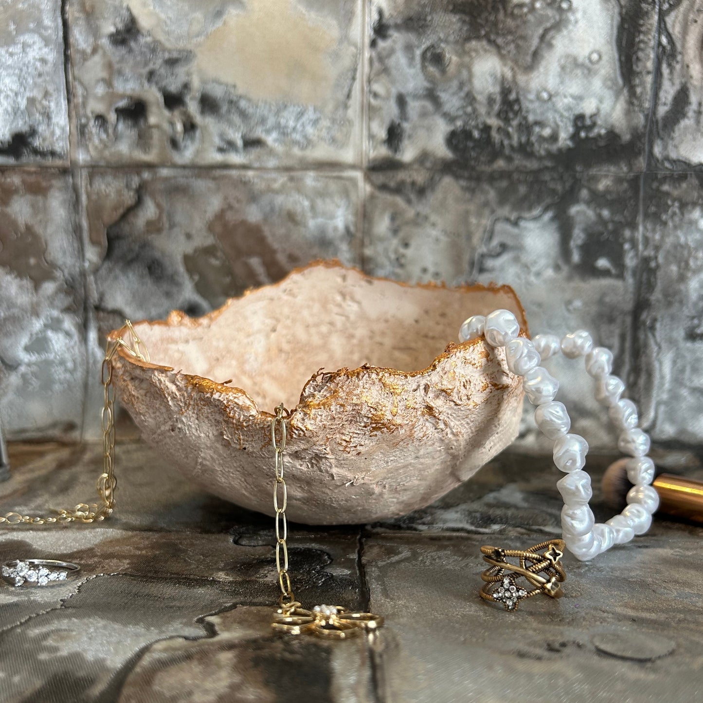 Handmade rustic bowl used as a jewelry holder, styled with pearls and gold rings.