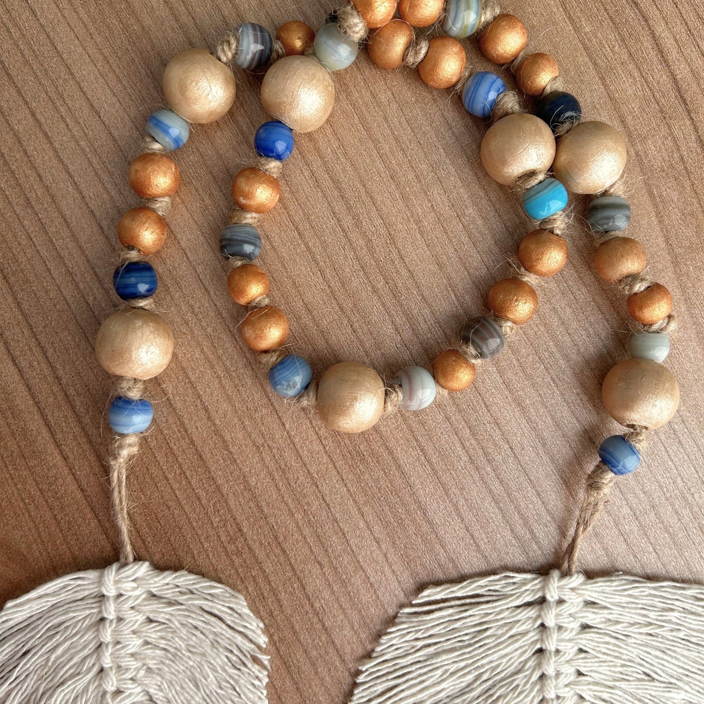 Detailed view of glass and wood beads in blue, grey, and gold tones with macrame leaves