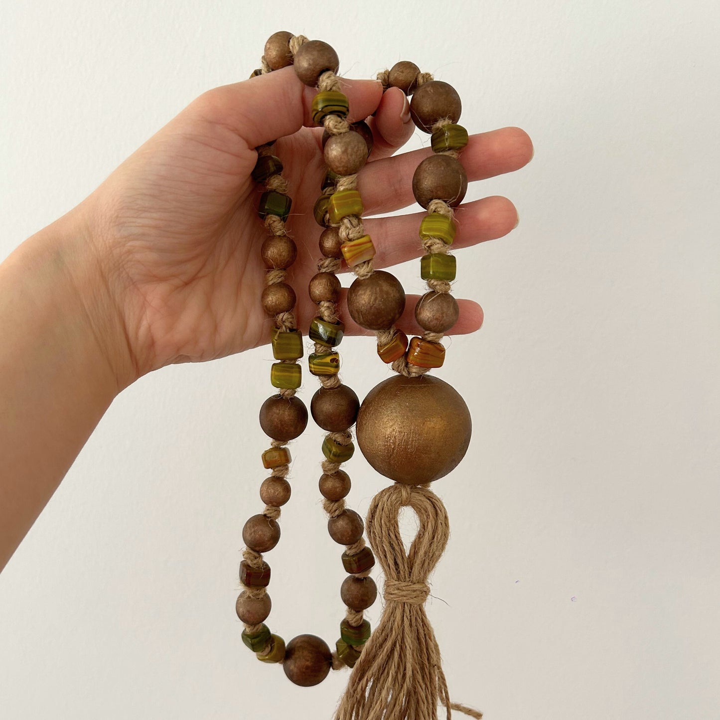 Artisan rustic bead garland with jute tassel shown in hand for scale.