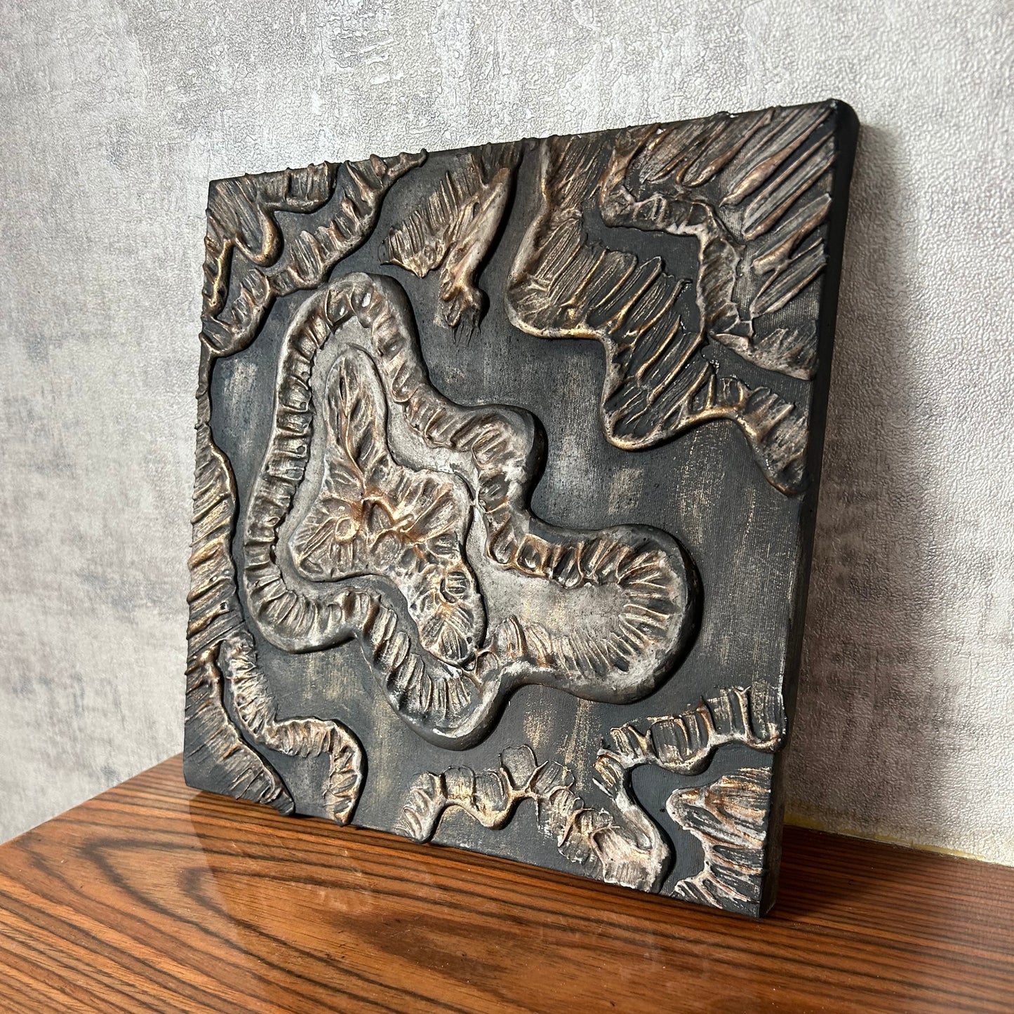 Side angle of textured wall art in earthy bronze and black tones on wooden surface