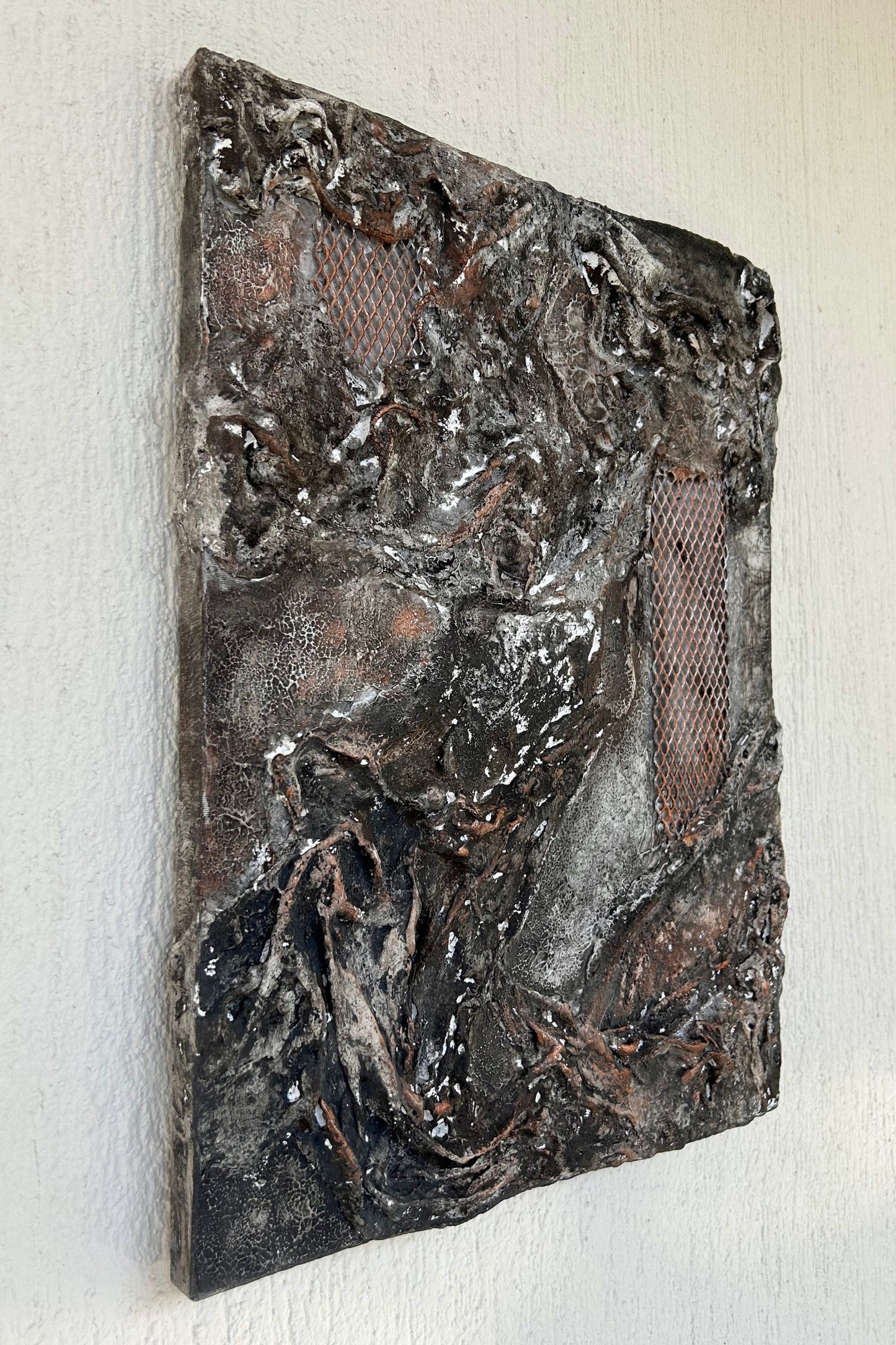 Close-up of cracked and aged plaster texture with embedded copper grid element.