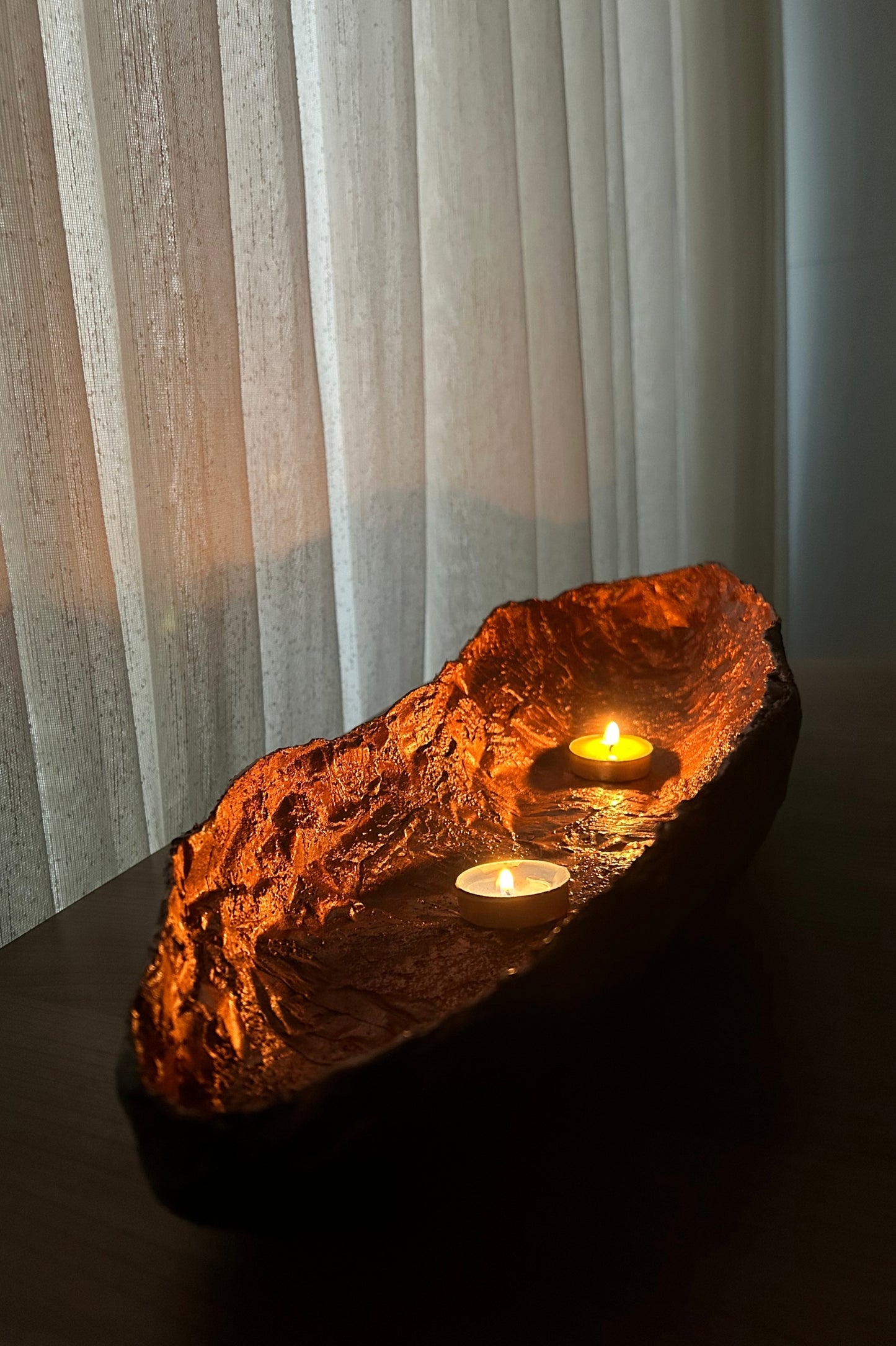 Handcrafted copper interior bowl on a dark wood surface with ambient light.