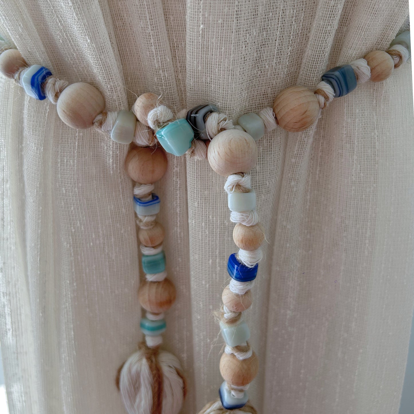 Bead garland styled as a curtain accent with round wooden beads and natural macrame texture.