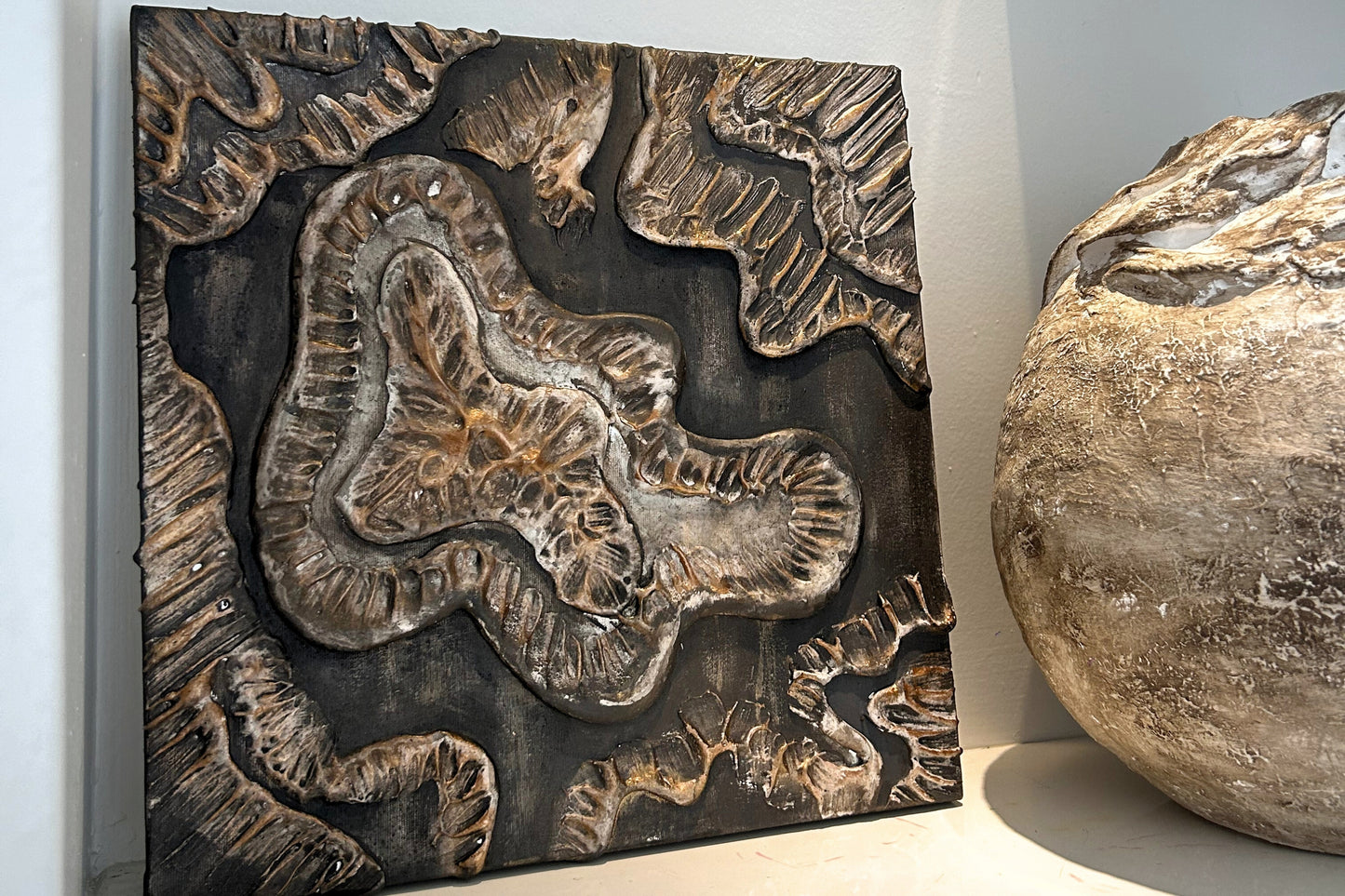 Two sculptural wall panels styled together near stone and pottery