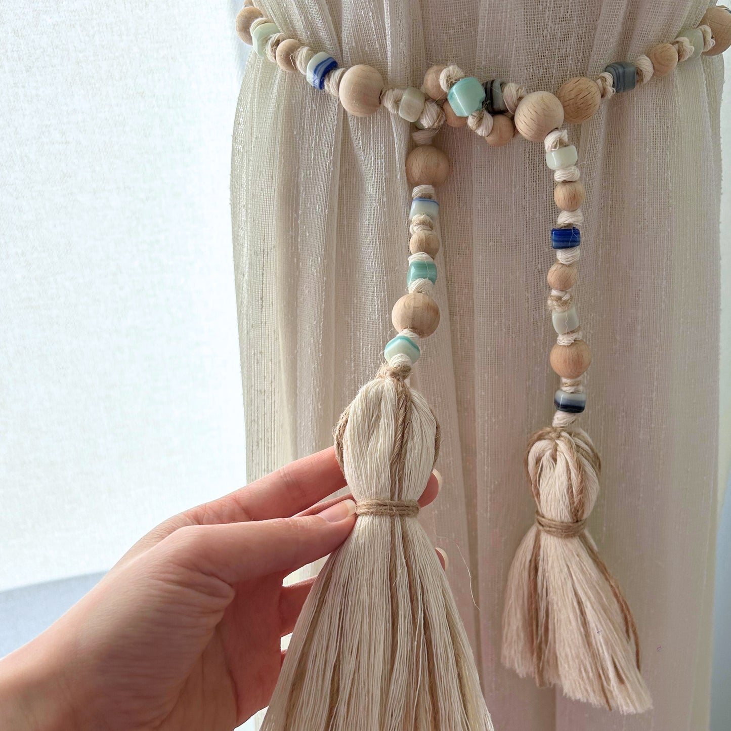 Hand holding rustic garland with jute tassels and handcrafted glass beads in earthy blue tones.