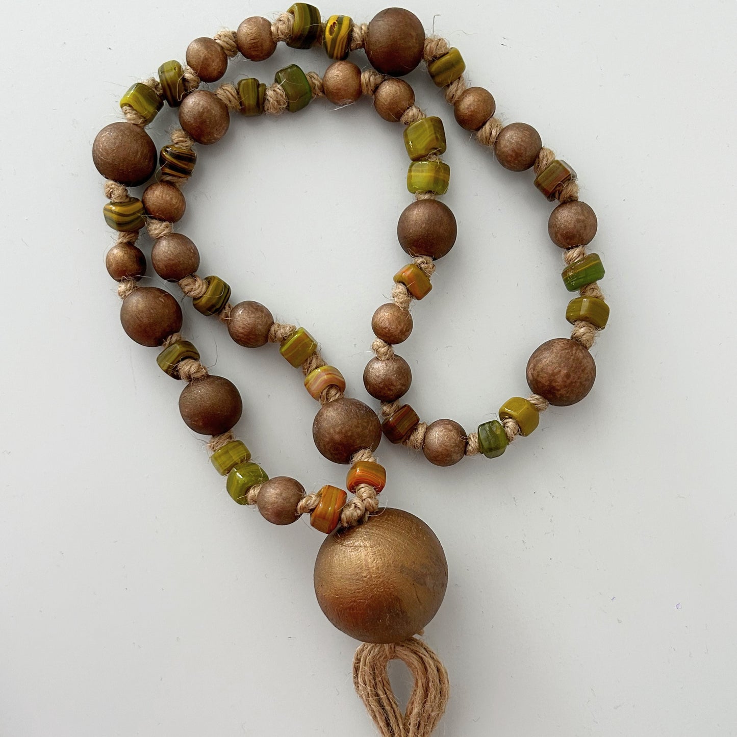 Oval arrangement of handmade rustic wooden and glass bead garland with jute tassel.