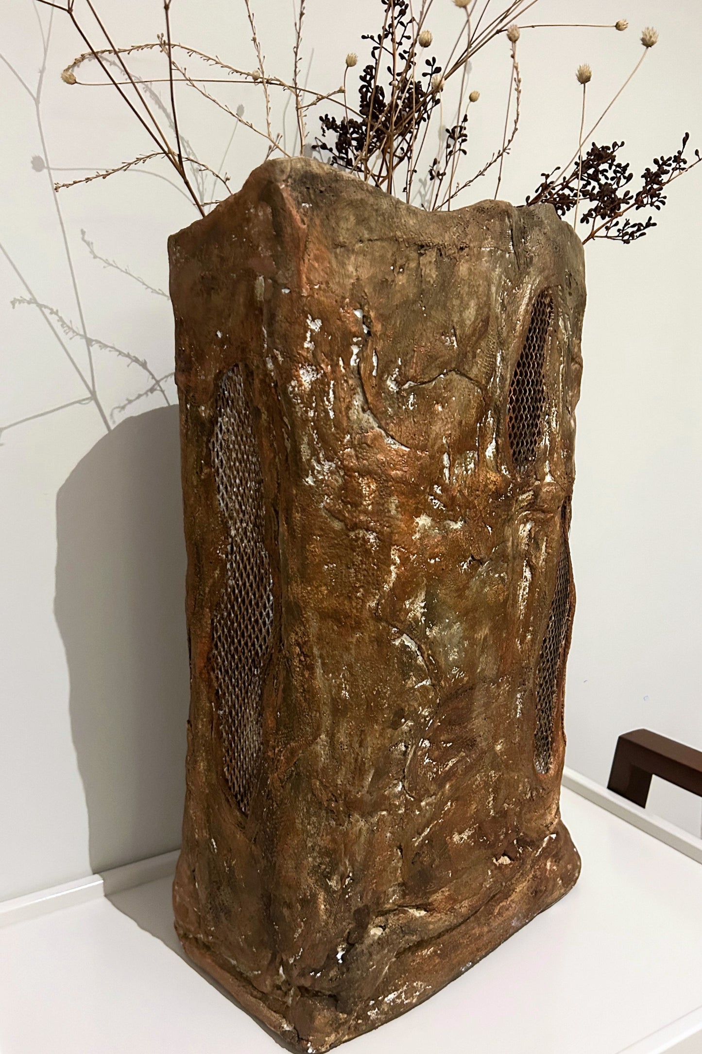 Side view of rustic paper mache floor vase styled with dried branches