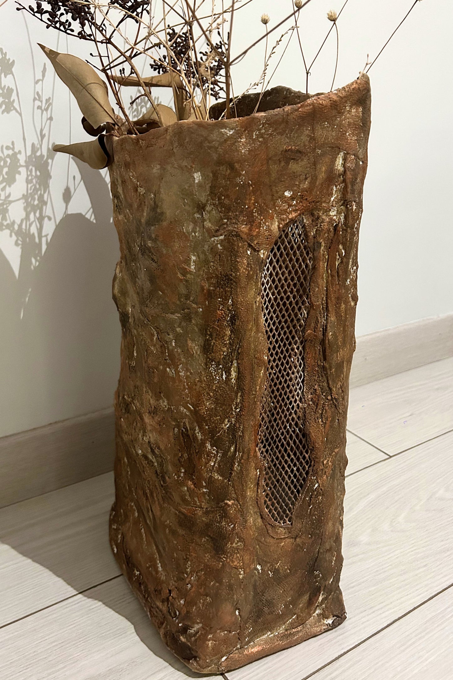 Back angled view of large earthy-toned handmade vase on white floor