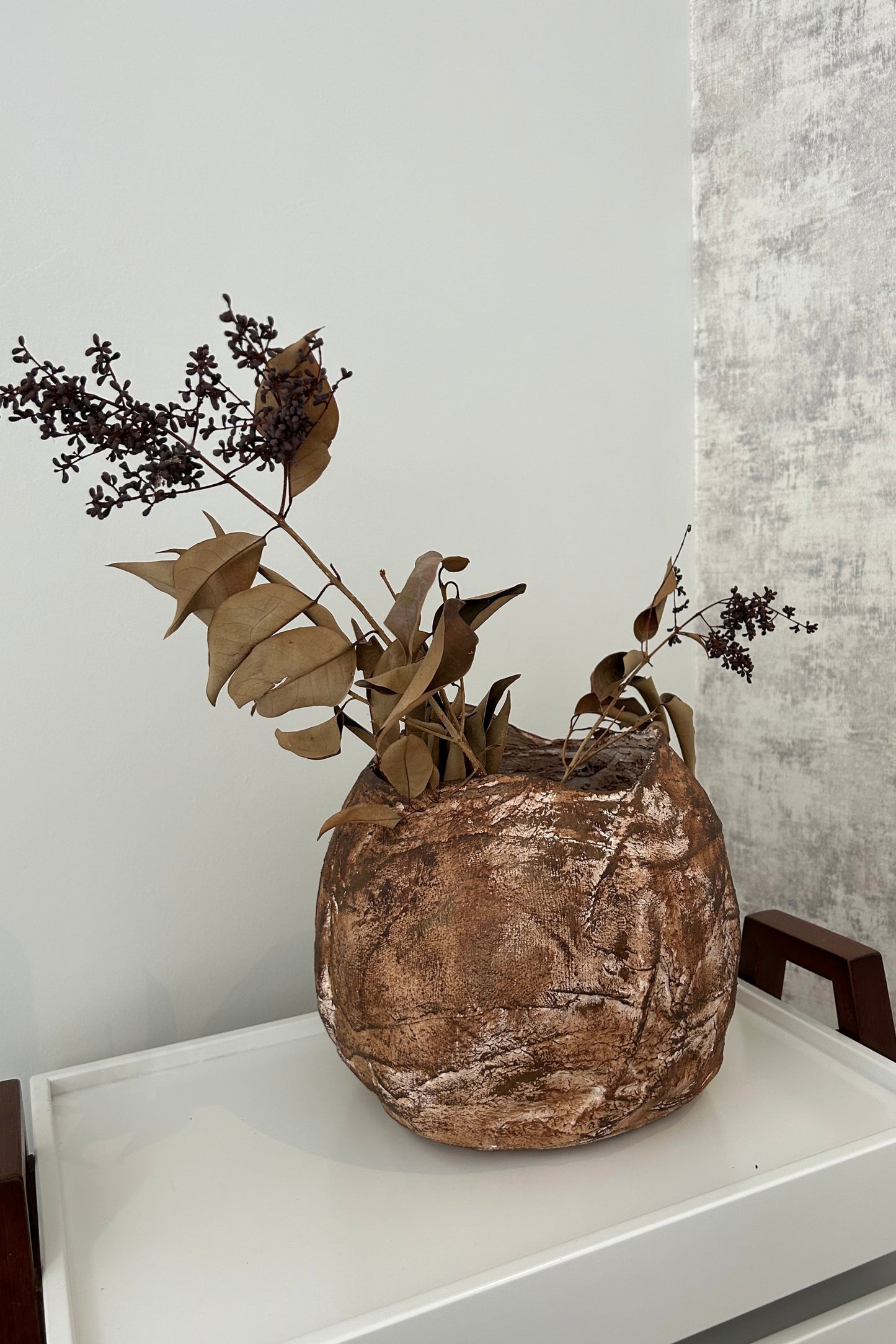 Large handmade wabi sabi vase styled with dried branches, placed beside a white wall for natural interior styling.