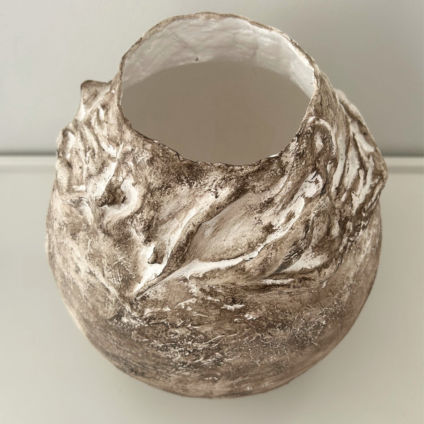 Close-up of sculpted rim with mineral texture and neutral finish on plaster vase.