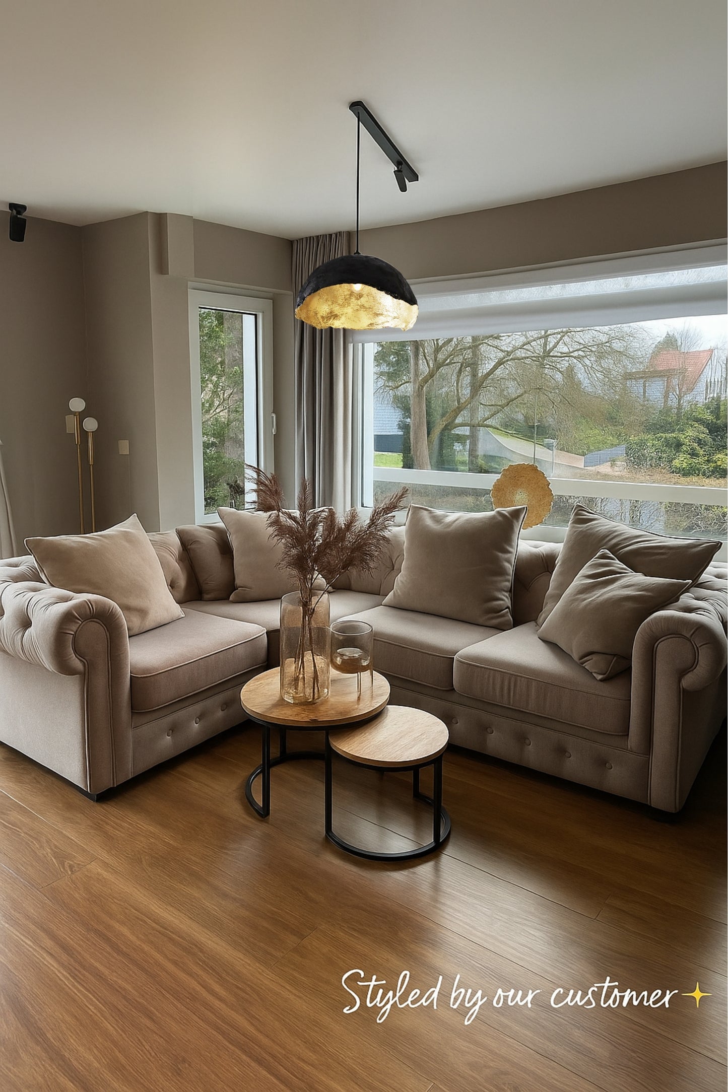 Customer-styled living room featuring a handmade gold shell pendant lamp hanging above a beige sectional sofa. The soft lighting and neutral tones create a cozy, modern interior