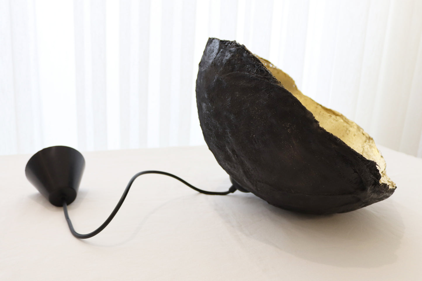 Side angle of hanging paper mache pendant lamp showing curved shell form