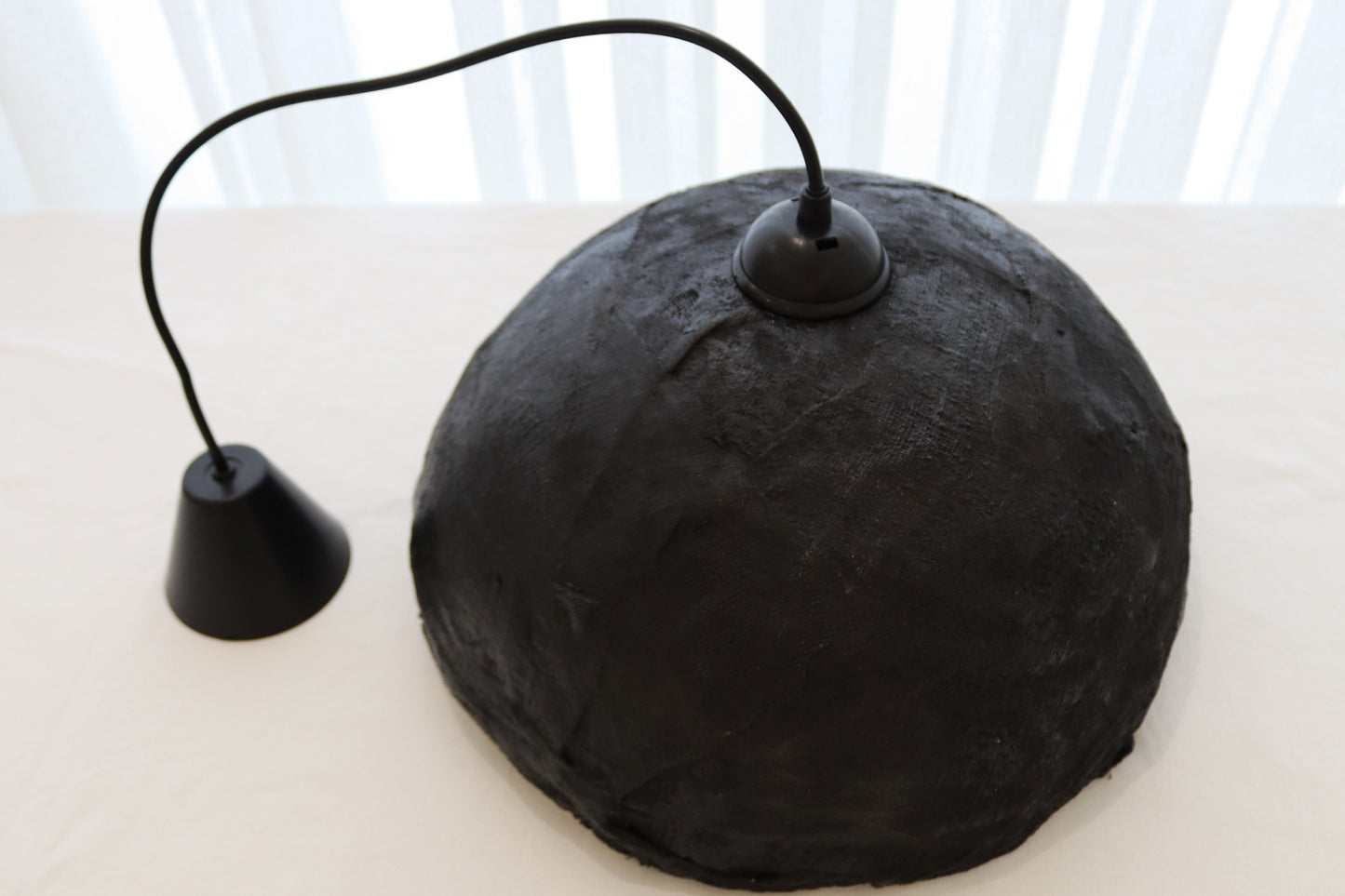 Back view of handmade black shell pendant light with cord visible on clean background