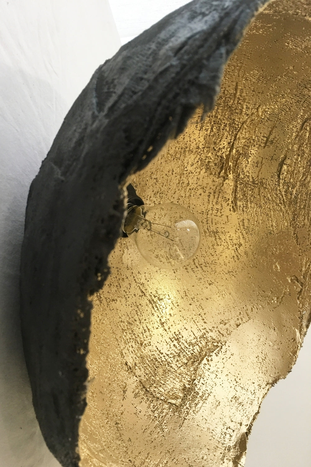 Close-up of textured surface showing gold interior and matte black exterior of paper mache pendant lamp