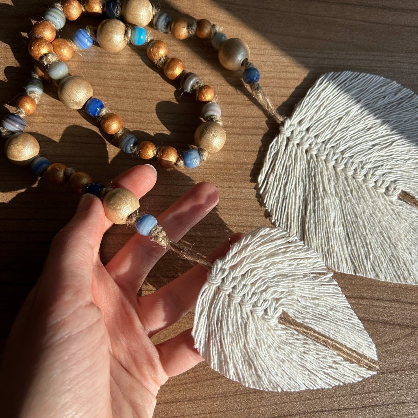 Human hand holding rustic garland with glass beads and jute macramé leaf tassels
