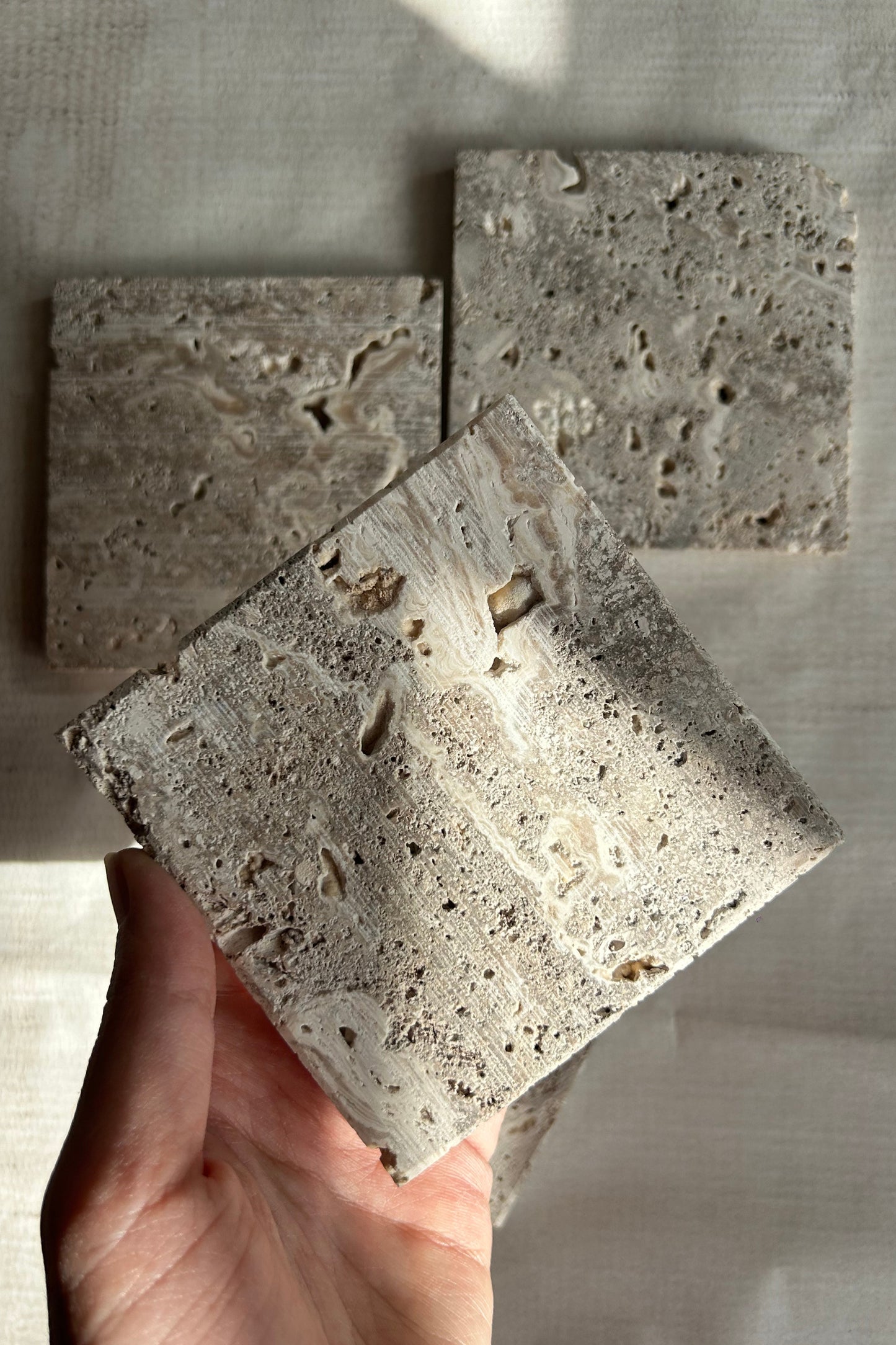 Close-up of a hand holding a square travertine photo prop
