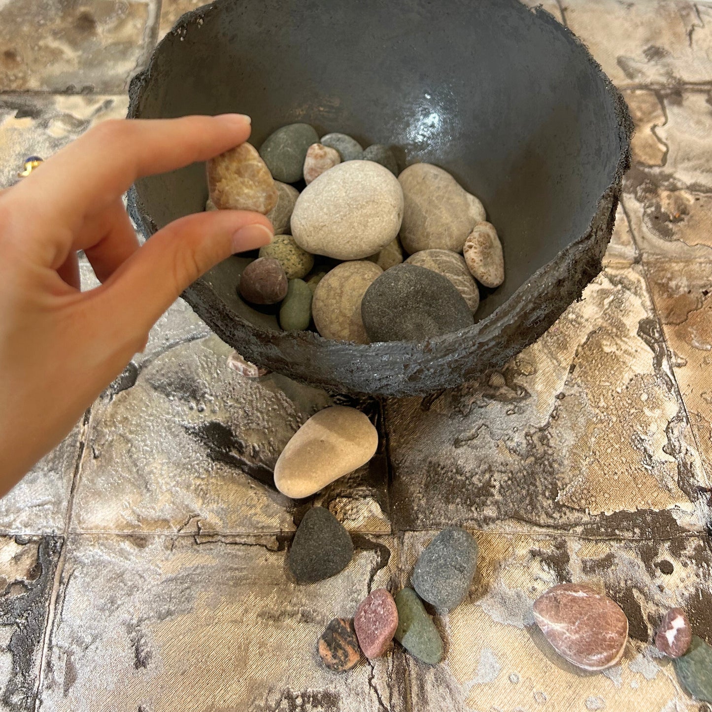 A hand holding a stone over the rustic handmade wabi sabi bowl.
