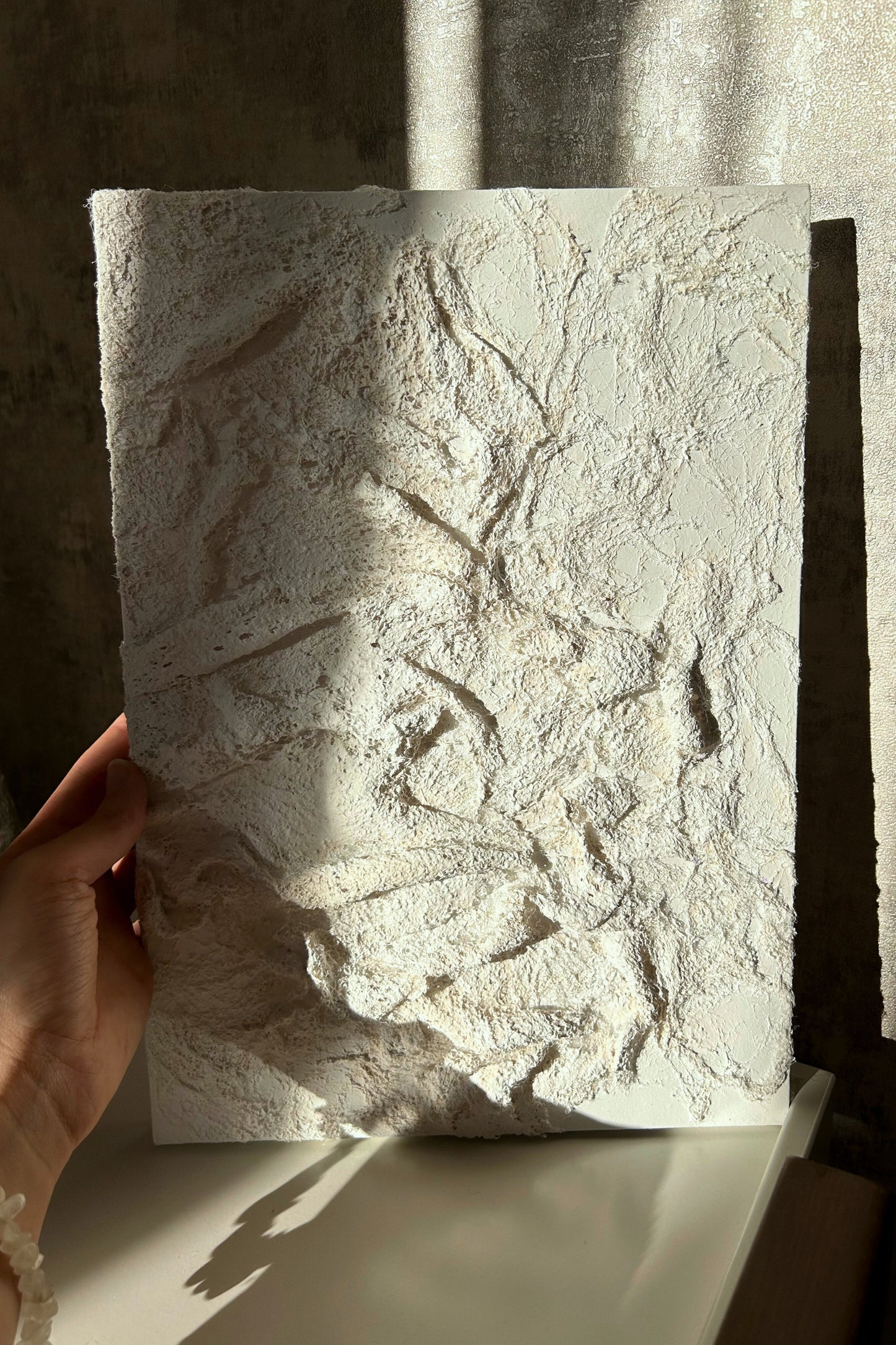 Artisan holding the ocean-inspired white plaster wall art with layered texture details.