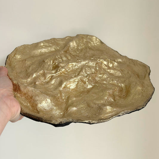 Organic handmade gold dish held up against a neutral background