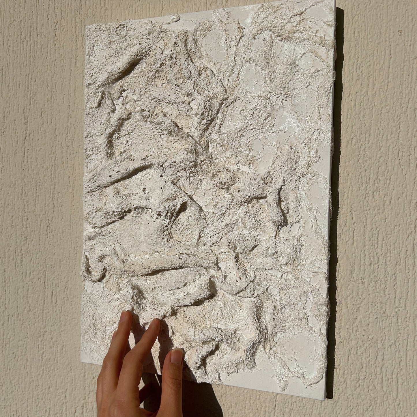 Hand gently touching the detailed plaster surface of the handmade textured wall decor.