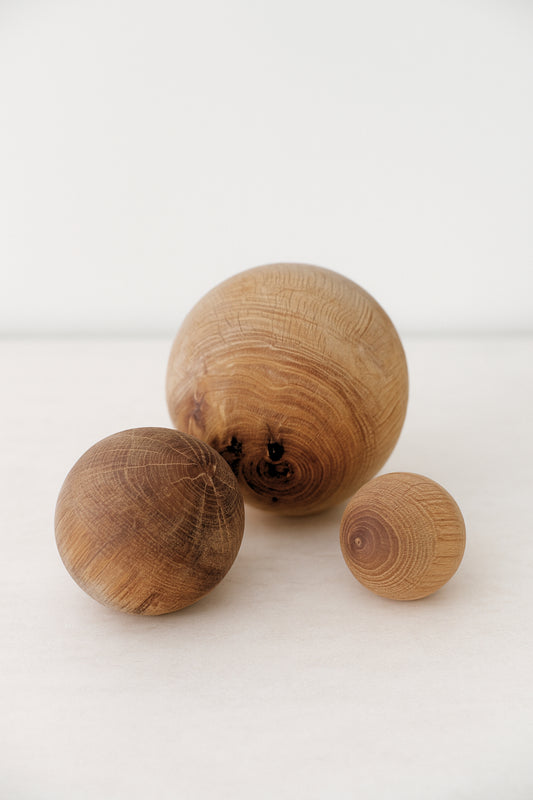 Close-up of three hand-carved wooden spheres in small, medium, and large sizes, highlighting natural grain and texture on a light neutral background.