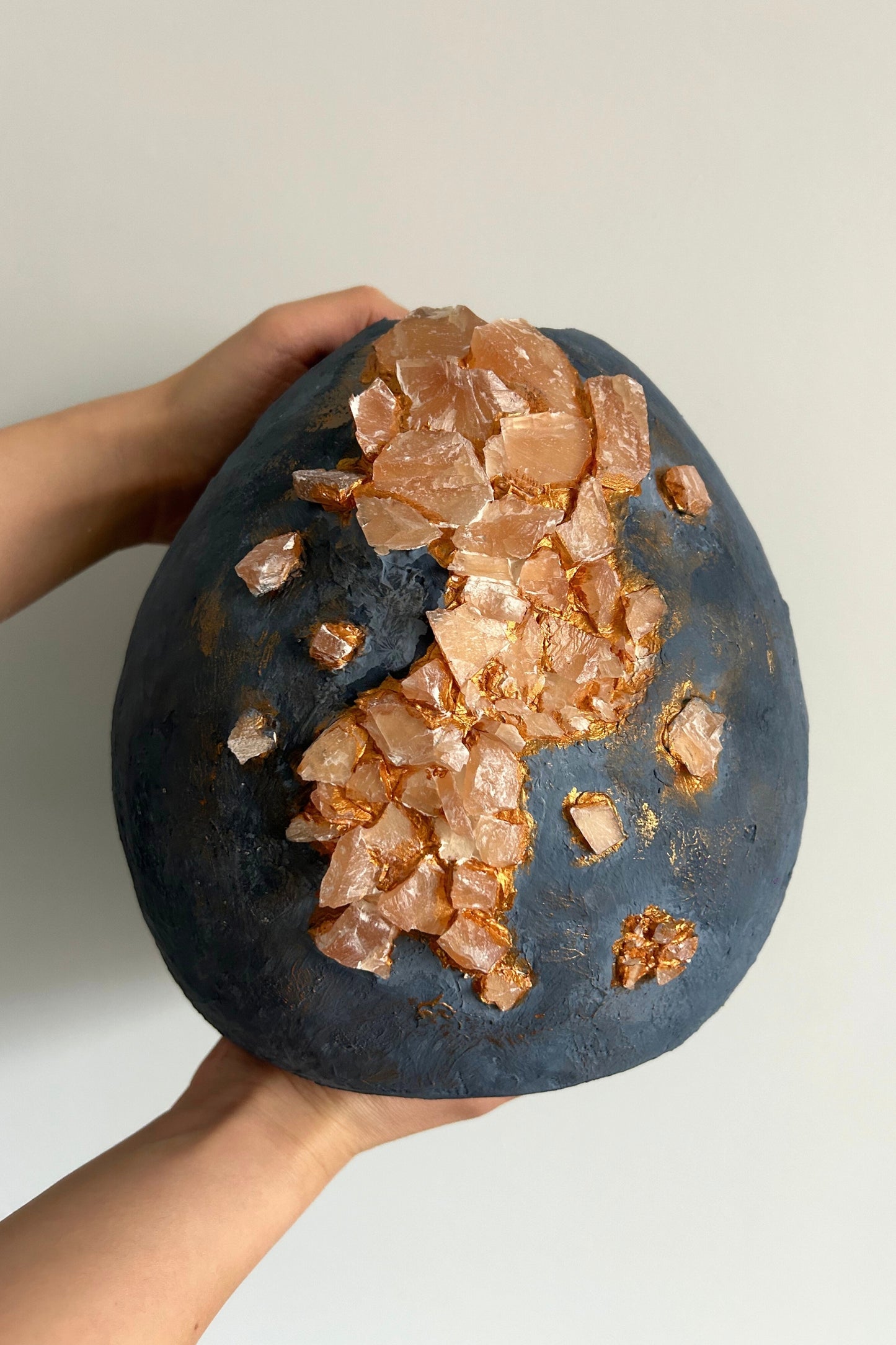 Hand-holding angle of sculptural blue vase with natural stones