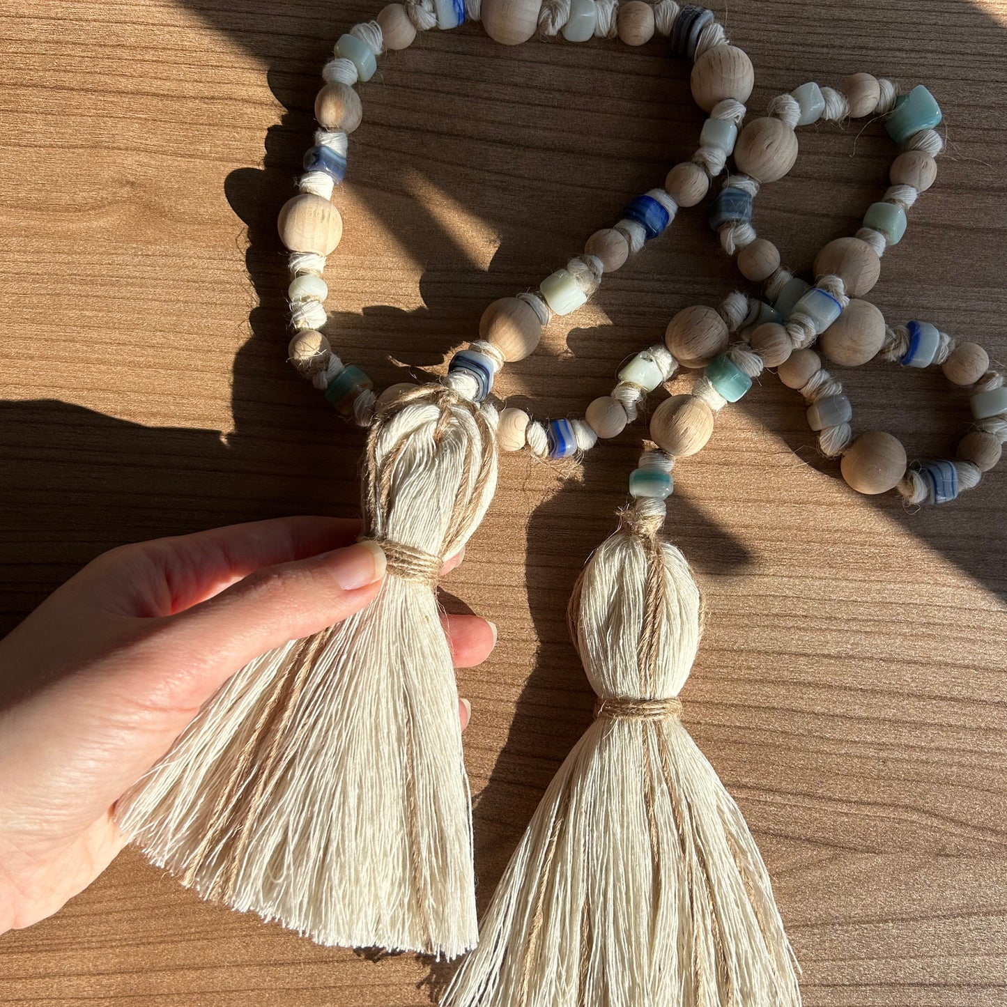 Warm-toned photo of handmade garland with jute tassels, casting soft shadows on wood surface.