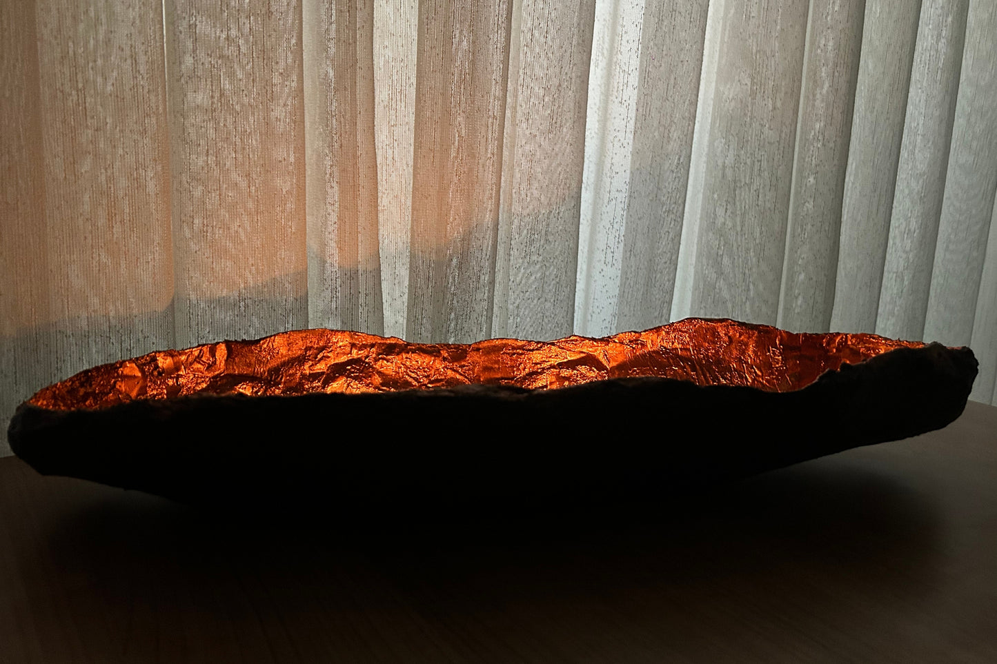 Close-up of textured copper wabi sabi bowl near soft curtains and natural sunlight.