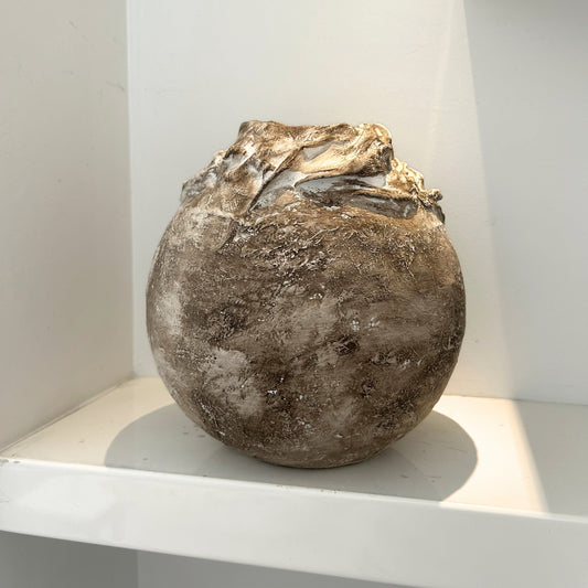 Handmade earthy brown vase with layered textures displayed on a white shelf.