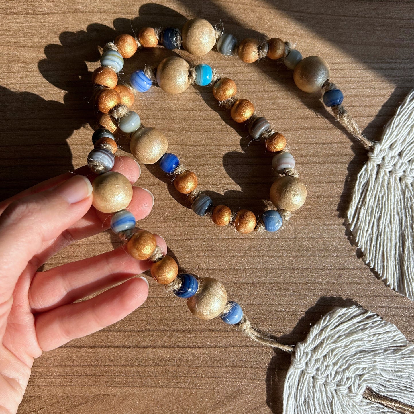 Hand showcasing golden wooden beads and deep blue glass beads on jute rope