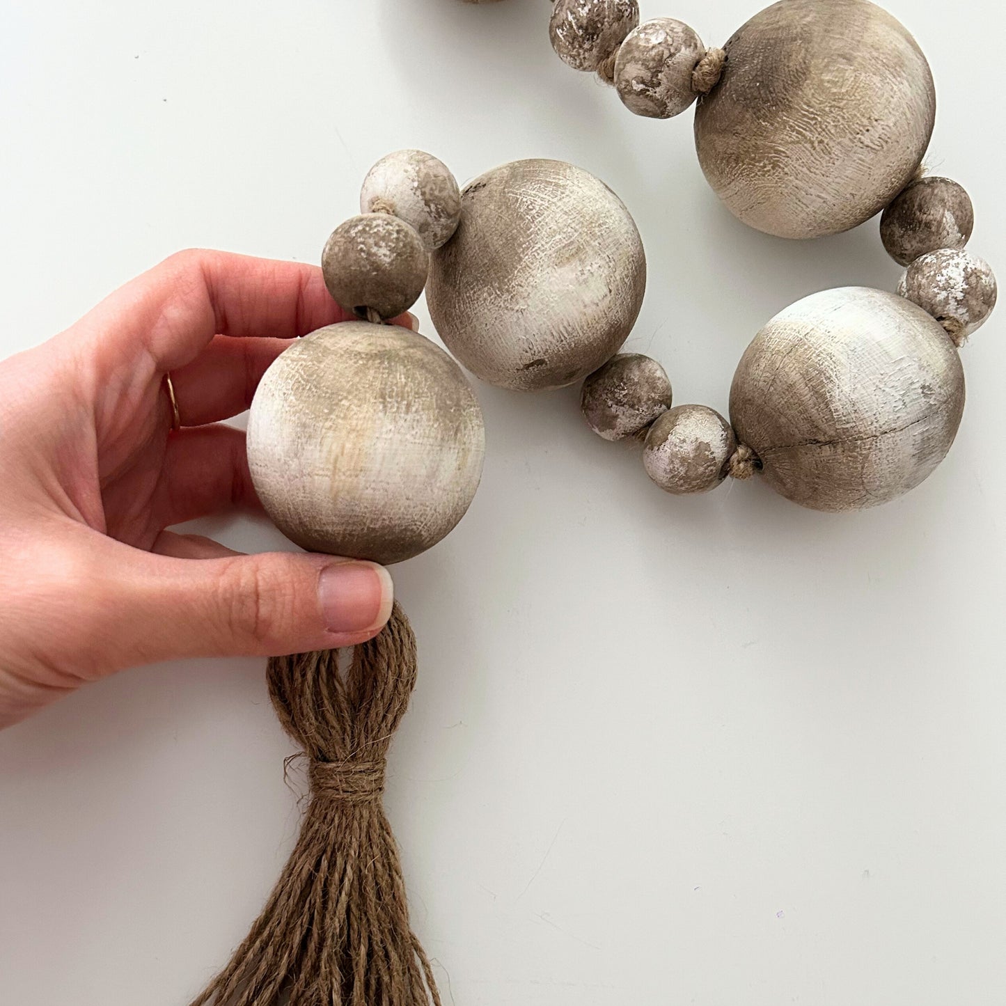 Hand holding rustic bead garland showing jute tassel detail