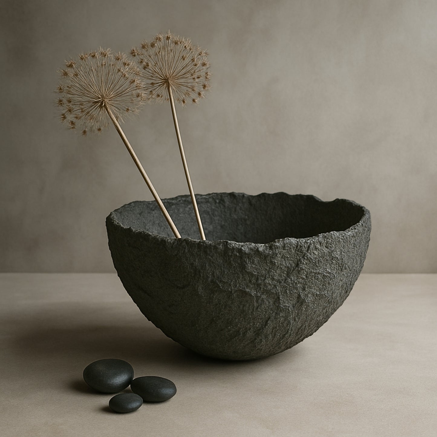 Sculptural black handmade bowl with dried flowers in a neutral, earthy setting.
