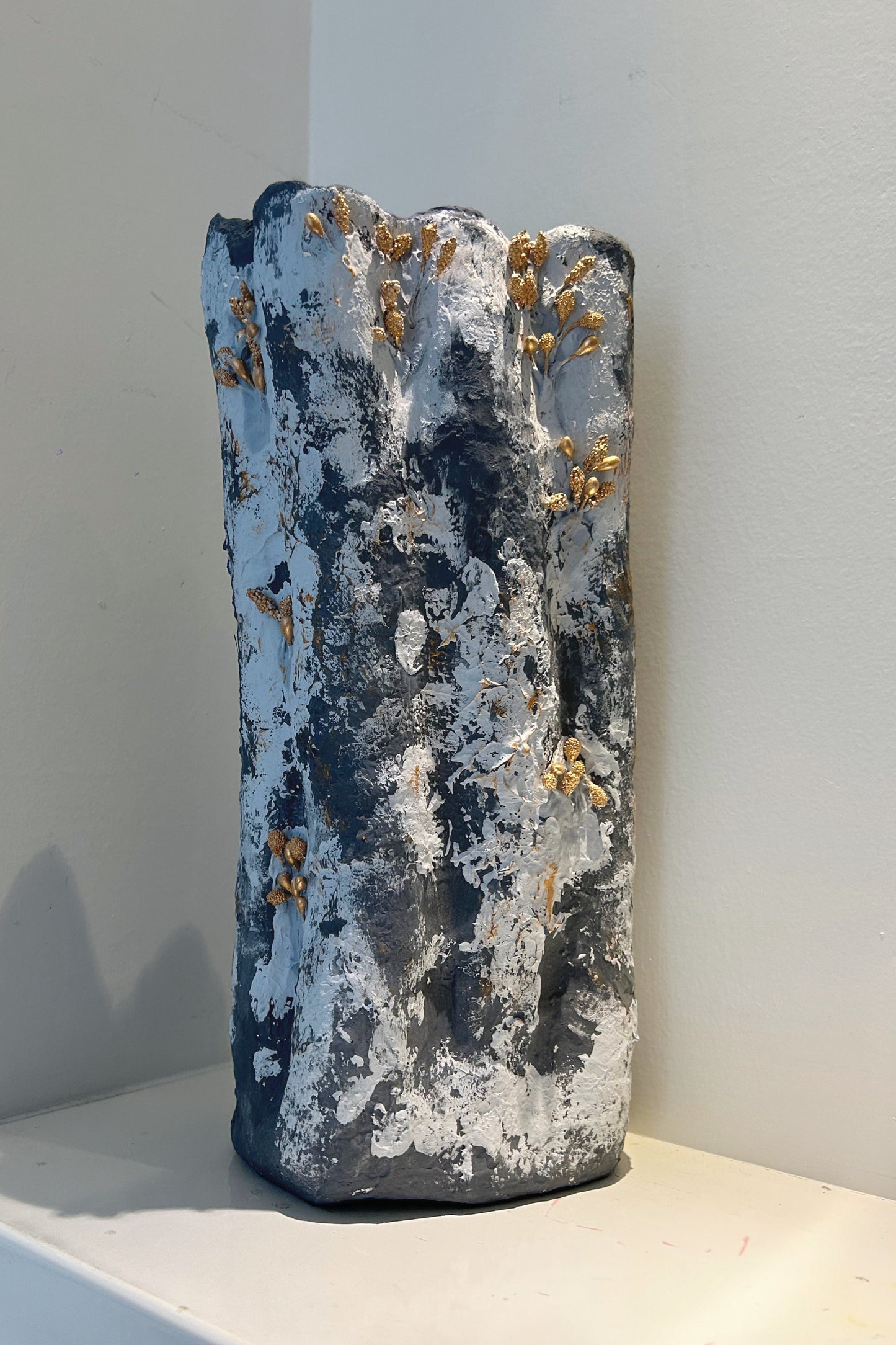 Handmade tall vase displayed on a shelf in a soft-lit modern interior, highlighting gold texture.