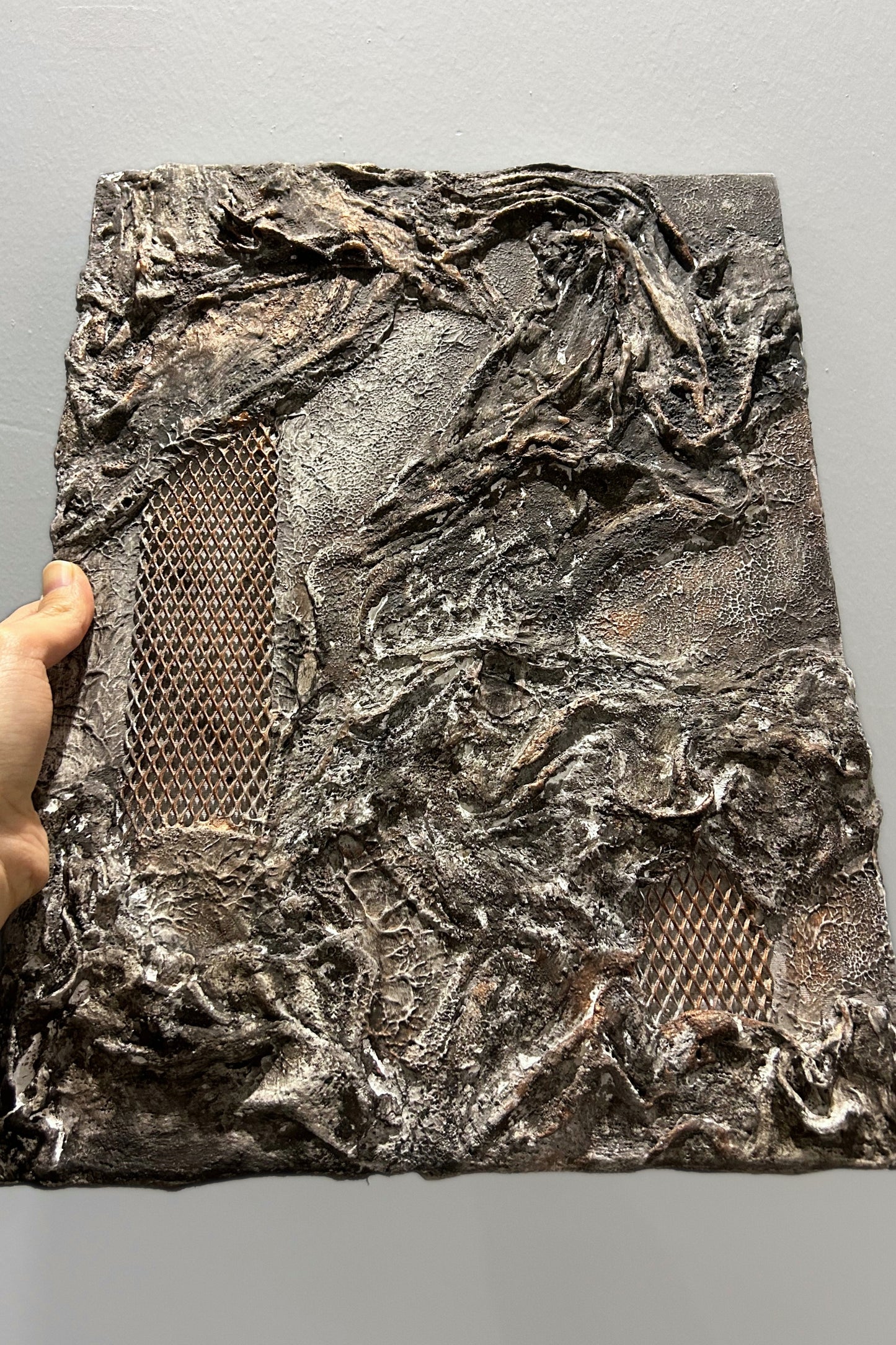 Sculptural wall panel from the front, displaying mixed textures and earthy black tones.
