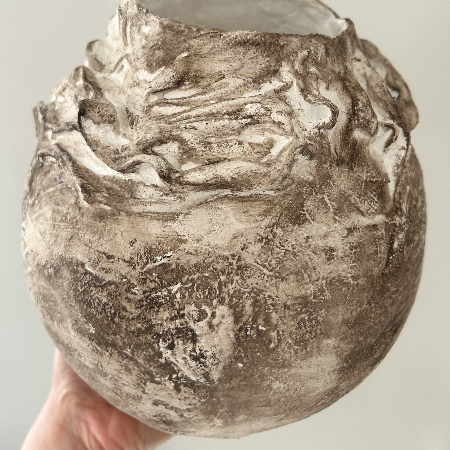Hand-holding large rustic vase with earthy plaster finish and organic form.