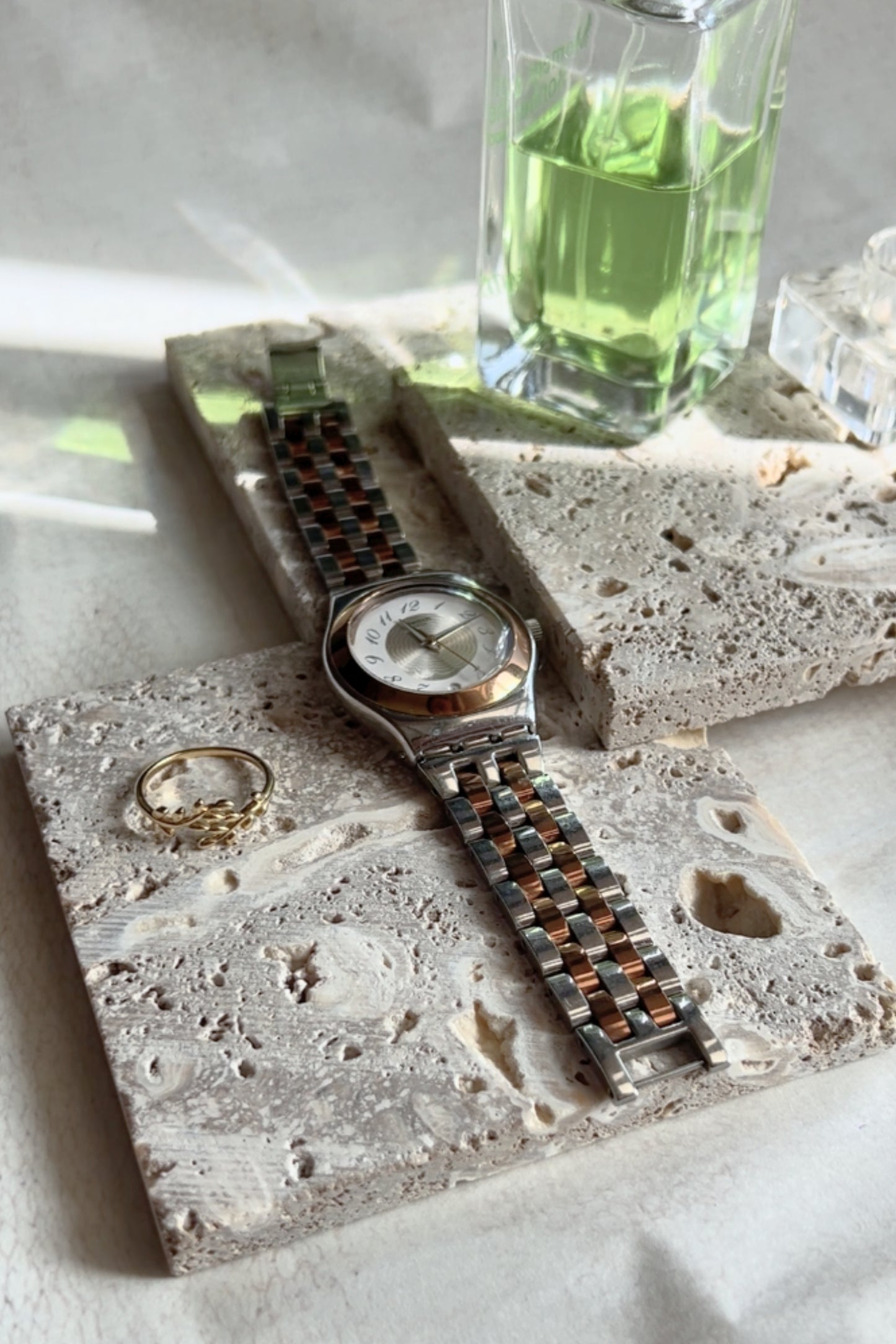 Green bottle and long necklace styled on layered travertine blocks