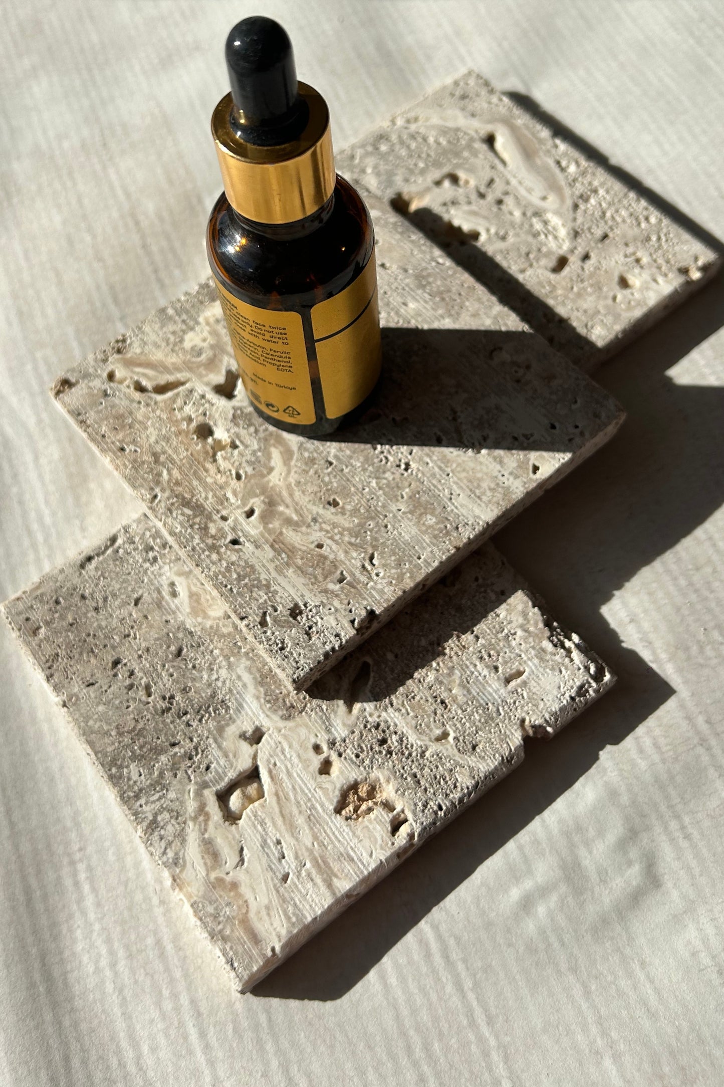 Small dropper bottle placed on beige travertine blocks in daylight