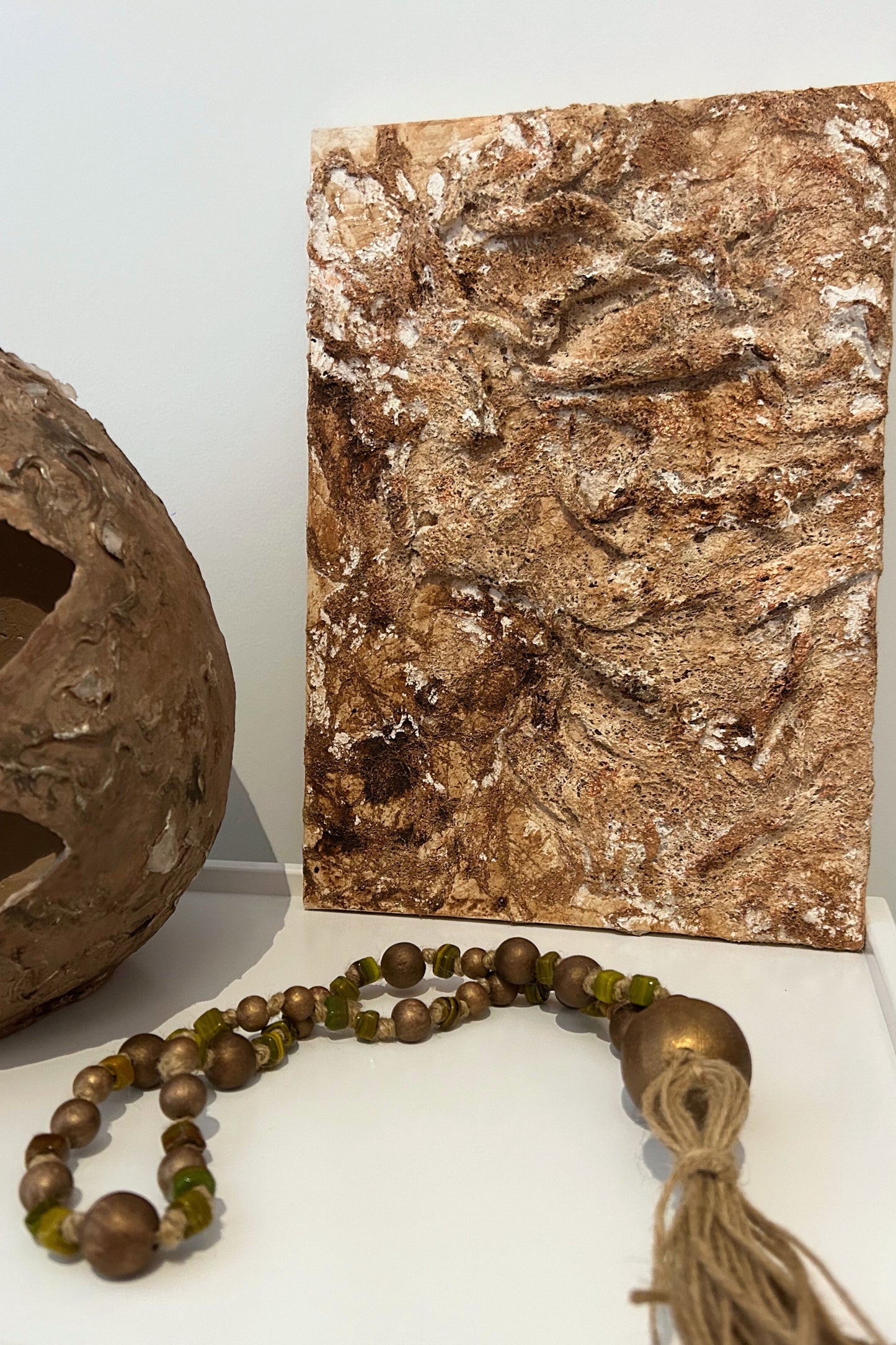 Rustic wall art styled next to natural ceramics and wooden beads in a Japandi setting.
