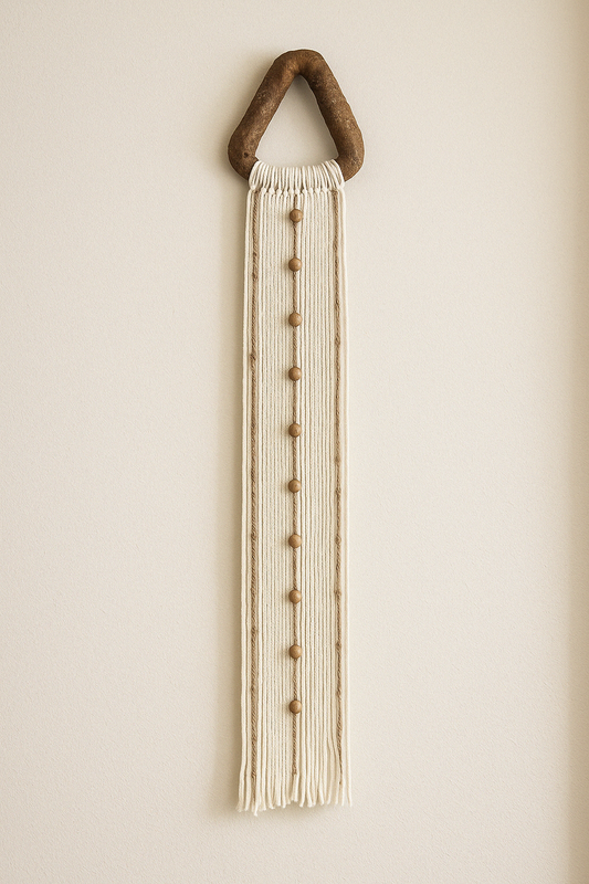 Long handmade yarn wall hanging styled on soft beige plaster wall.