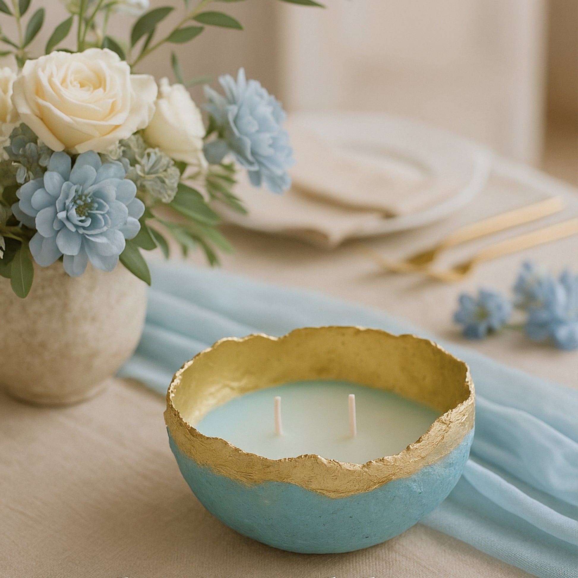 Handmade aqua blue and gold candle bowl placed on an elegant table with pastel blue flowers and beige tableware — perfect for rustic or boho wedding decor.