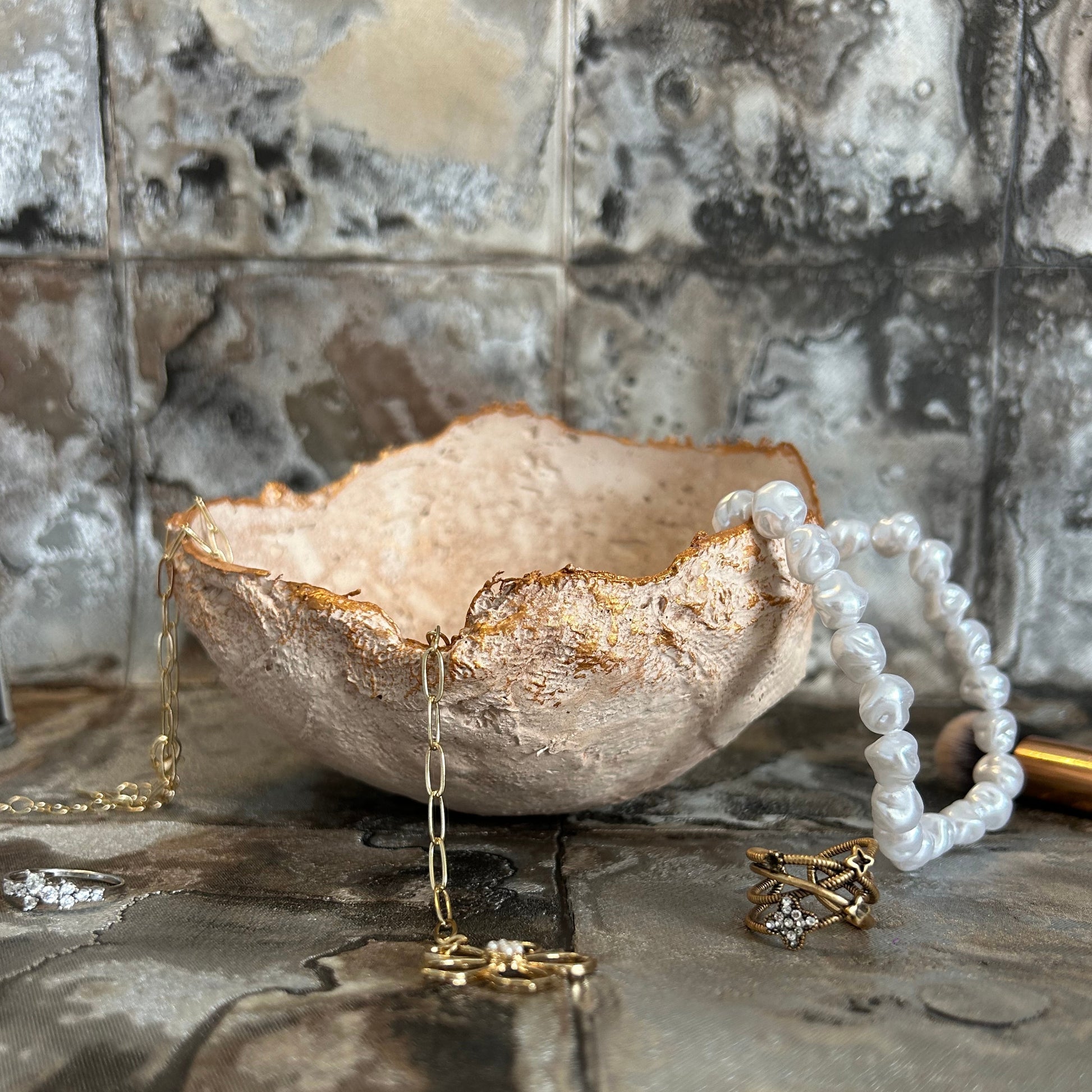 Handmade rustic bowl used as a jewelry holder, styled with pearls and gold rings.