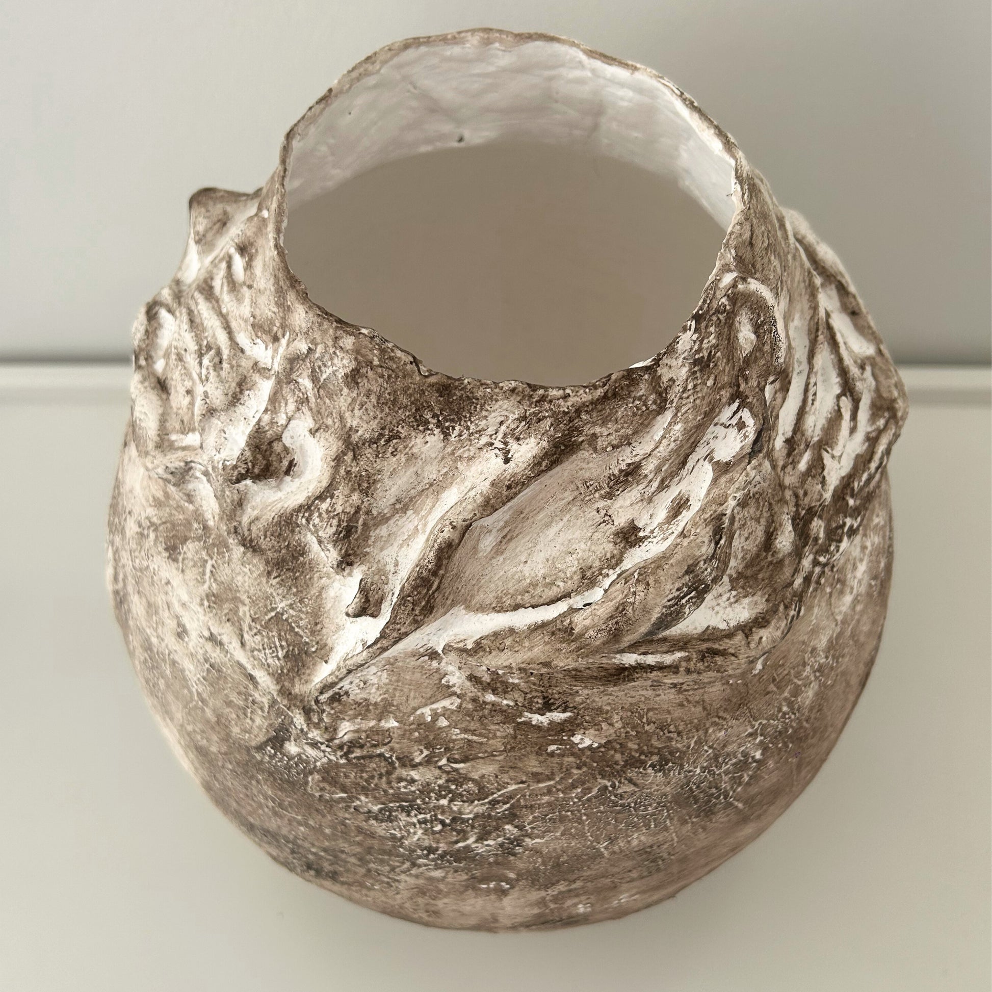 Close-up of sculpted rim with mineral texture and neutral finish on plaster vase.