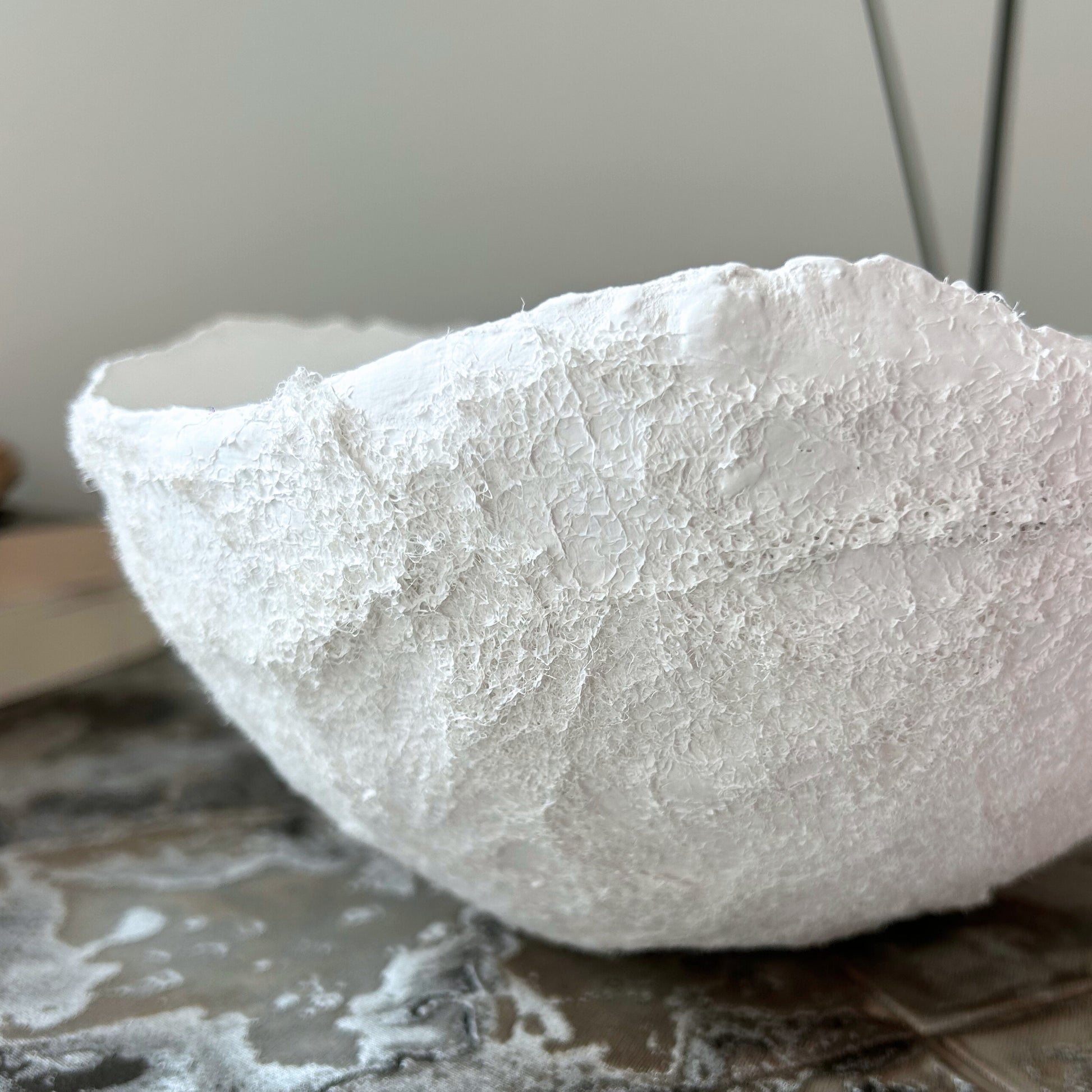 Zoom on the surface detail of a textured white bowl, catching sunlight to reveal organic imperfections