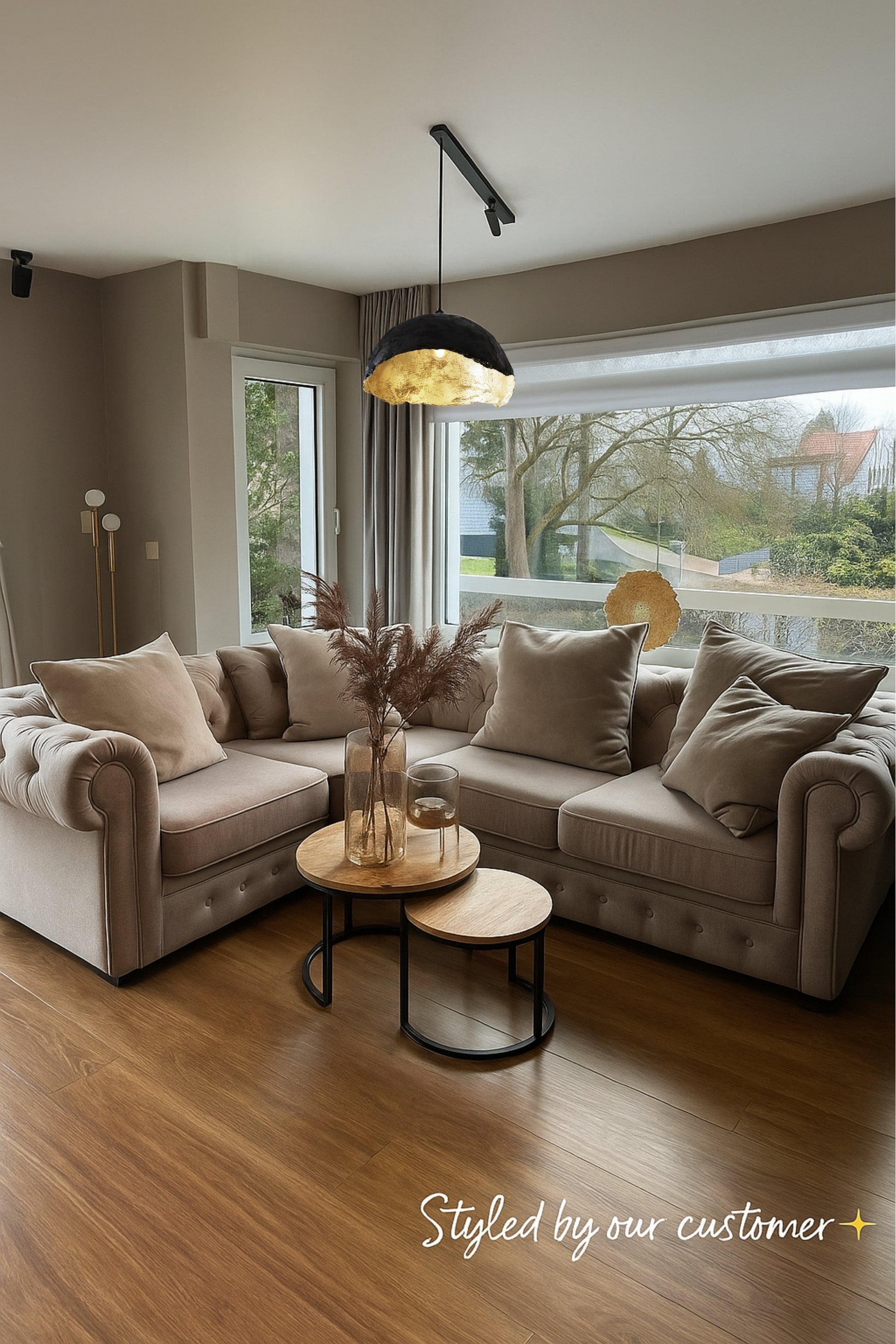 Customer-styled living room featuring a handmade gold shell pendant lamp hanging above a beige sectional sofa. The soft lighting and neutral tones create a cozy, modern interior