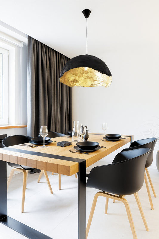 Handmade gold-lined pendant lamp hanging over a modern dining table. The black and gold design adds warmth and elegance to a minimal, contemporary space.