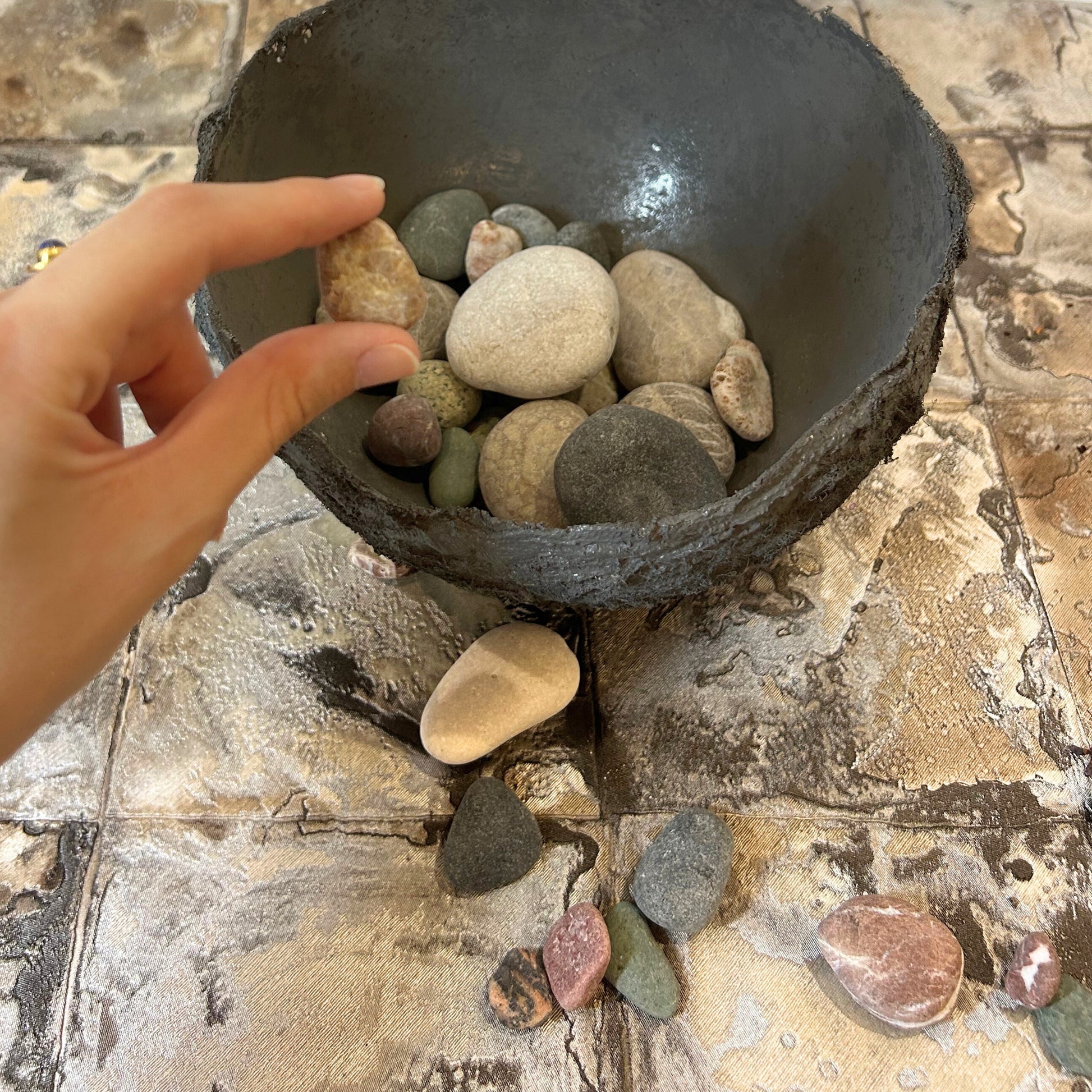 A hand holding a stone over the rustic handmade wabi sabi bowl.