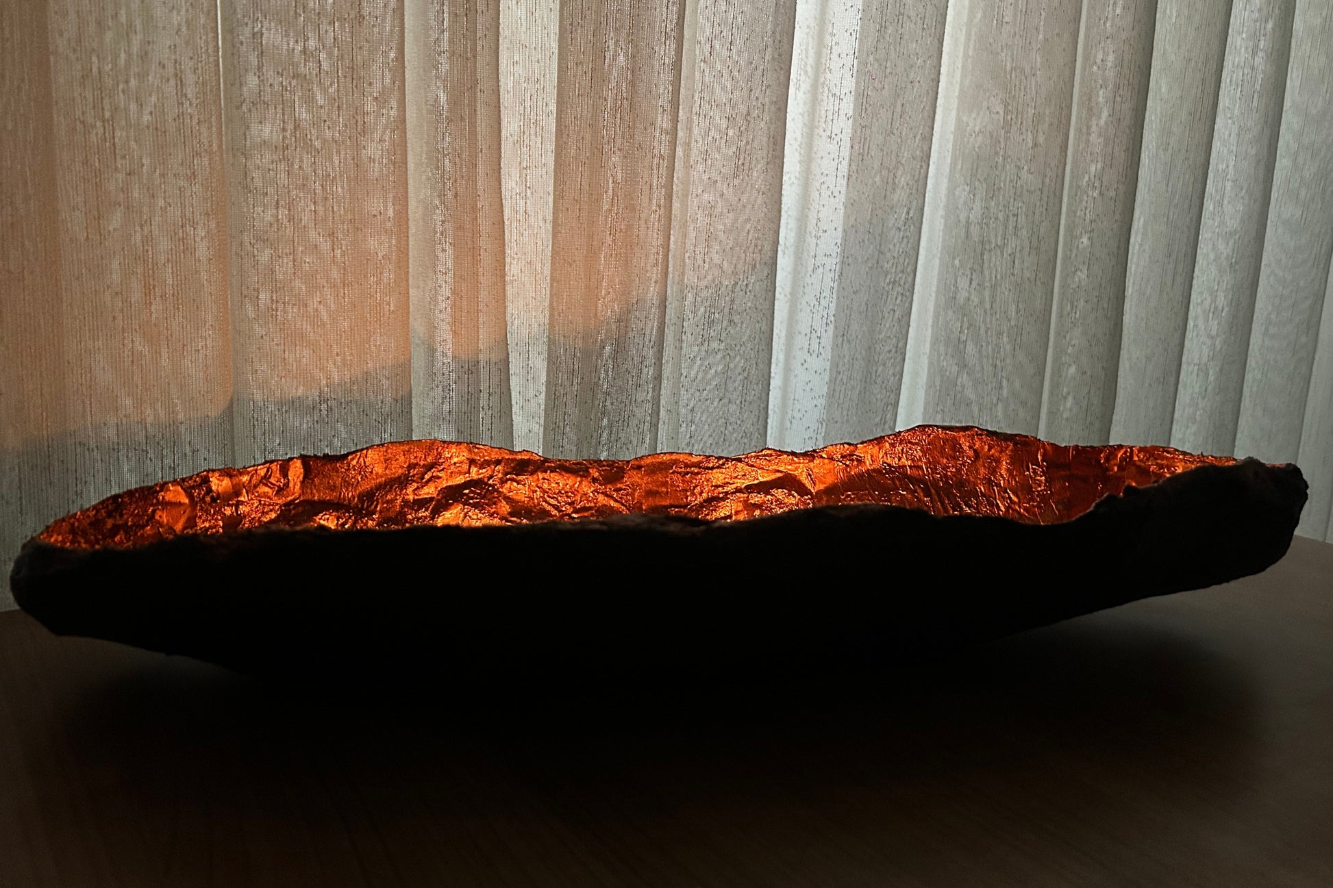 Close-up of textured copper wabi sabi bowl near soft curtains and natural sunlight.